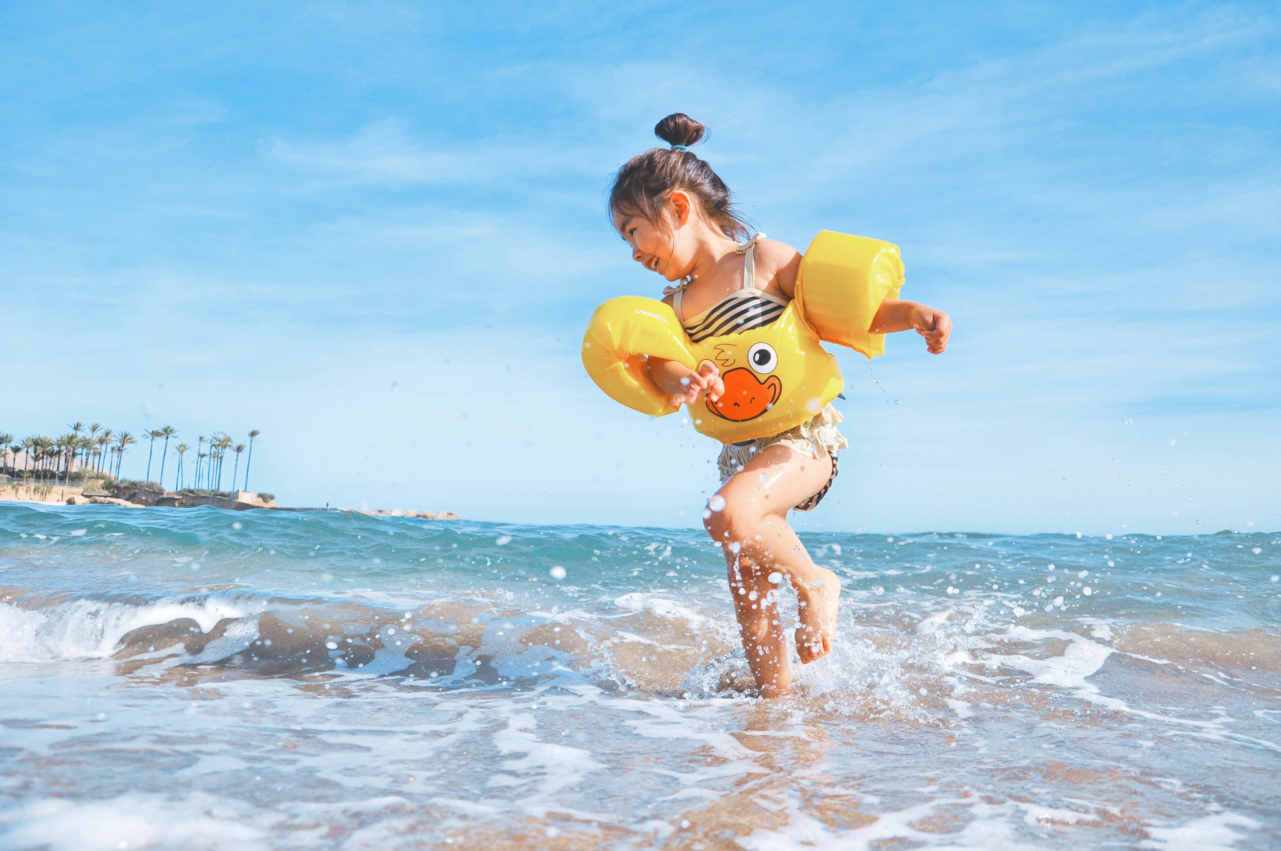 Summer Vacation 桌布 壁紙 — 一個快樂的孩子穿著黃色鴨仔水泡在蔚藍天空下跑過海浪。