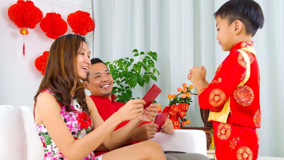 Red Envelope 桌布 壁紙 — 一個快樂的家庭慶祝農曆新年，父母給穿著喜慶紅色傳統服飾的微笑孩子派發紅包。