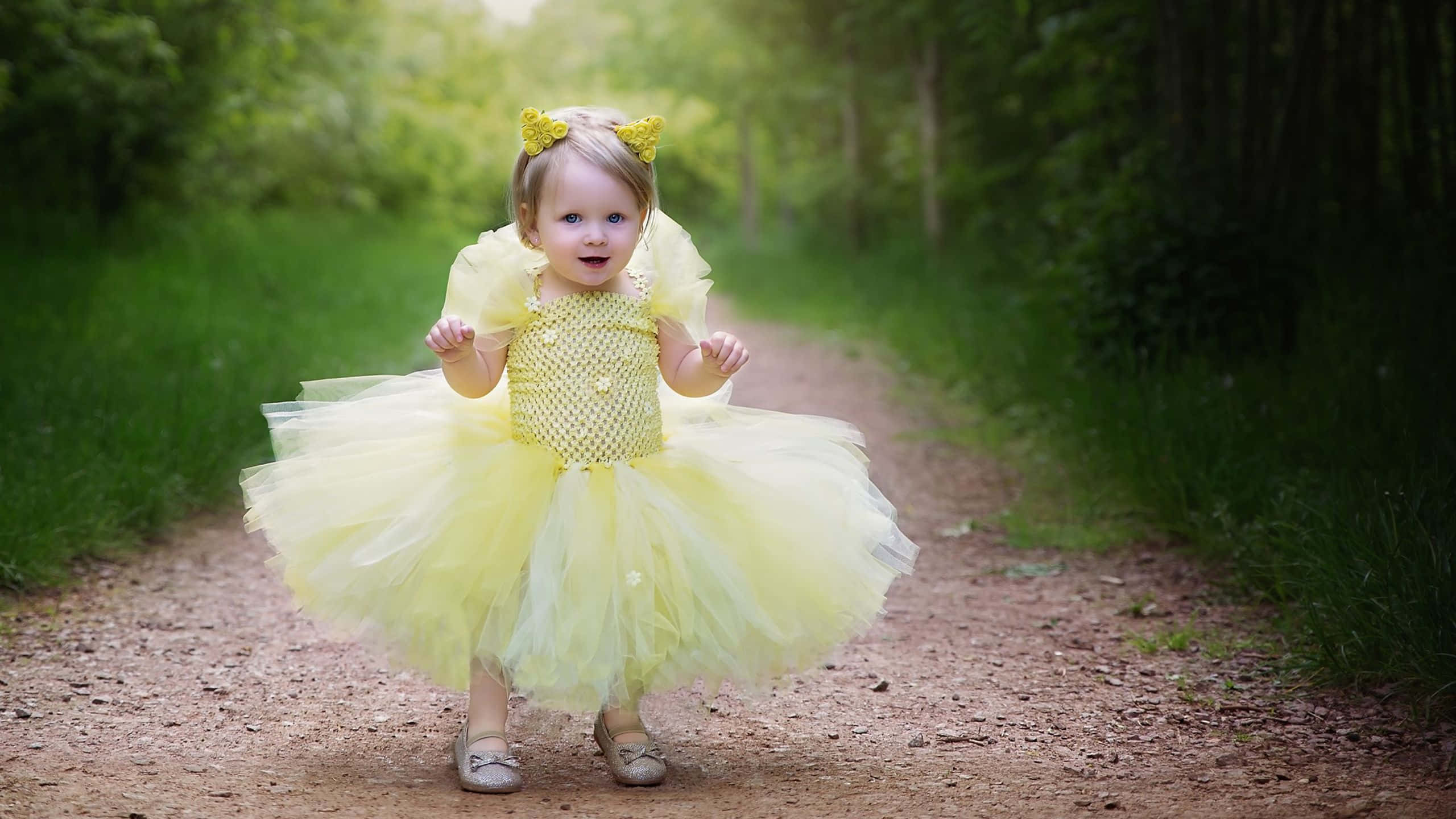 Yellow Dress 桌布 壁紙 — 一個快樂的幼兒穿著鮮黃色薄紗裙和相配的頭帶，走在陽光普照的森林小徑上。