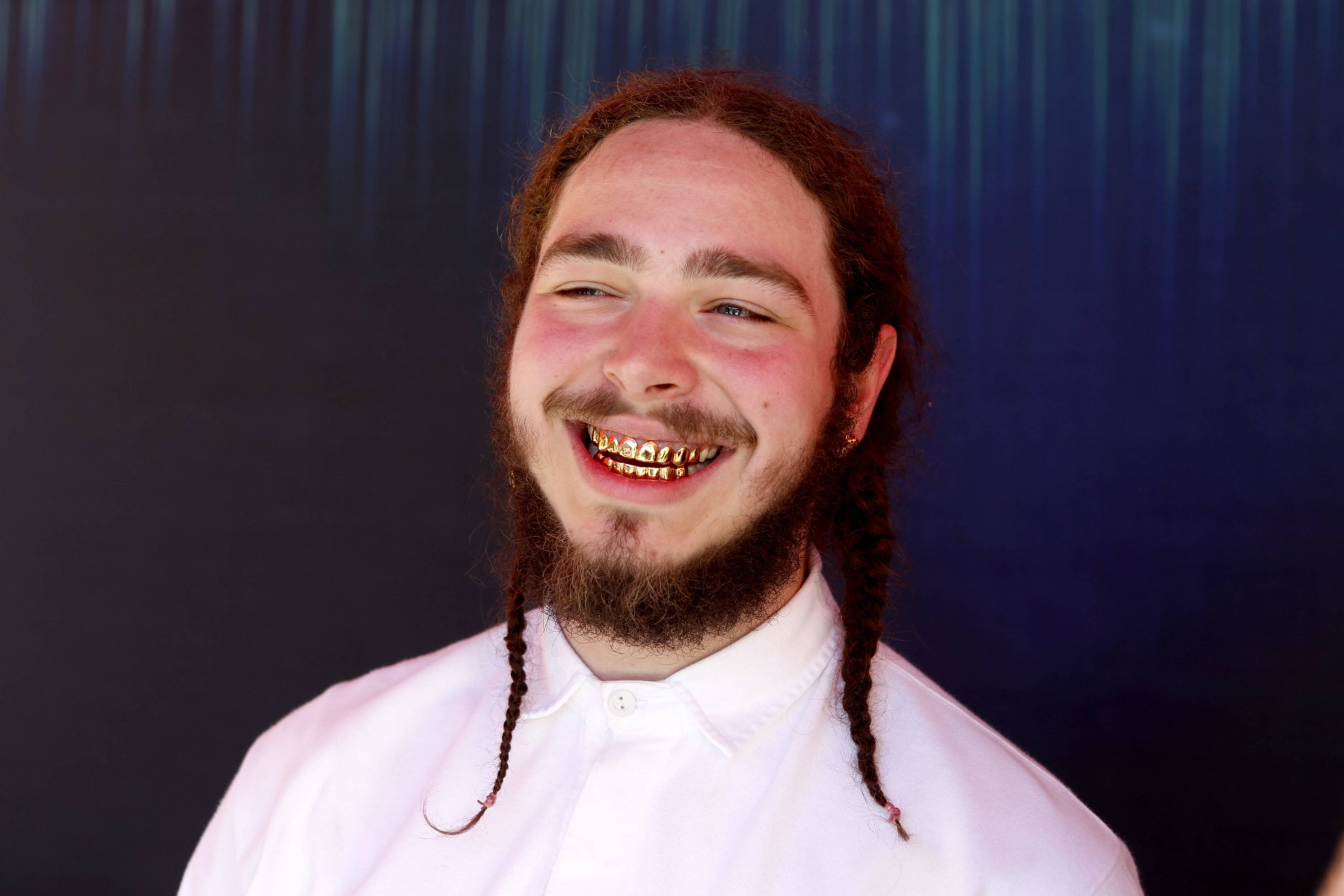 Post Malone Jagermeister Party 2016 壁紙 — 一個快樂的男人，辮子頭髮和金色牙套，在深藍色窗簾背景下燦爛地笑。