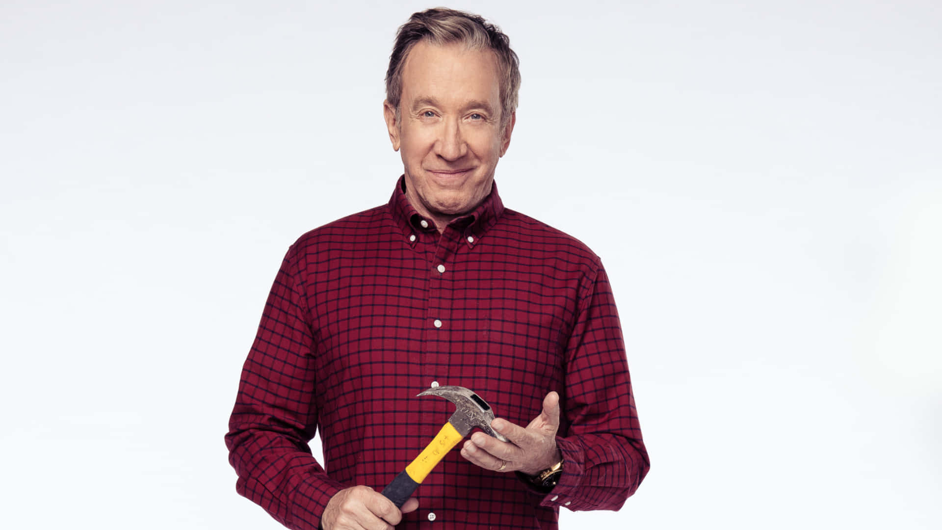 Tim Allen 桌布 壁紙 — 一個快樂的男人穿著紅色格仔恤衫，在純白色背景前拿著一把羊角錘。