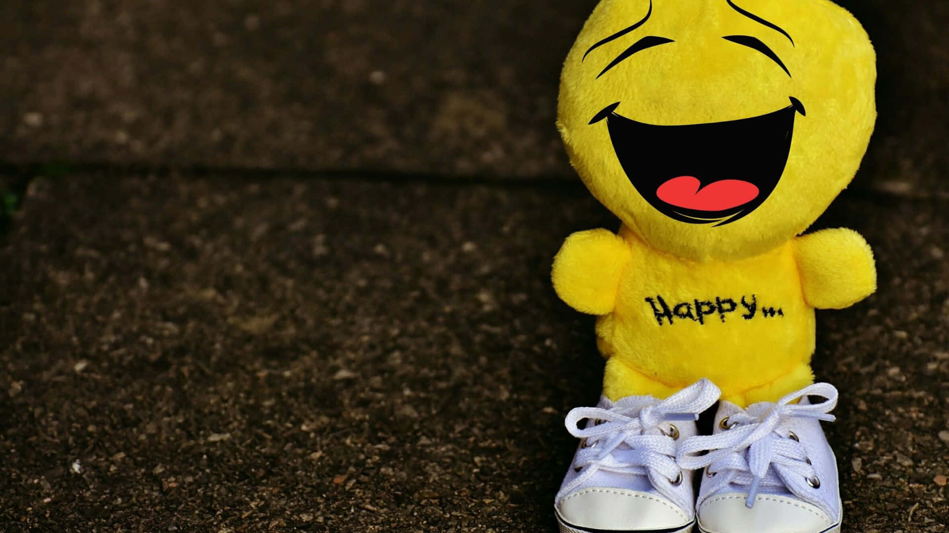 Smiley 桌布 壁紙 — 一個快樂的黃色表情公仔穿著白色運動鞋坐在有紋理的混凝土表面上。