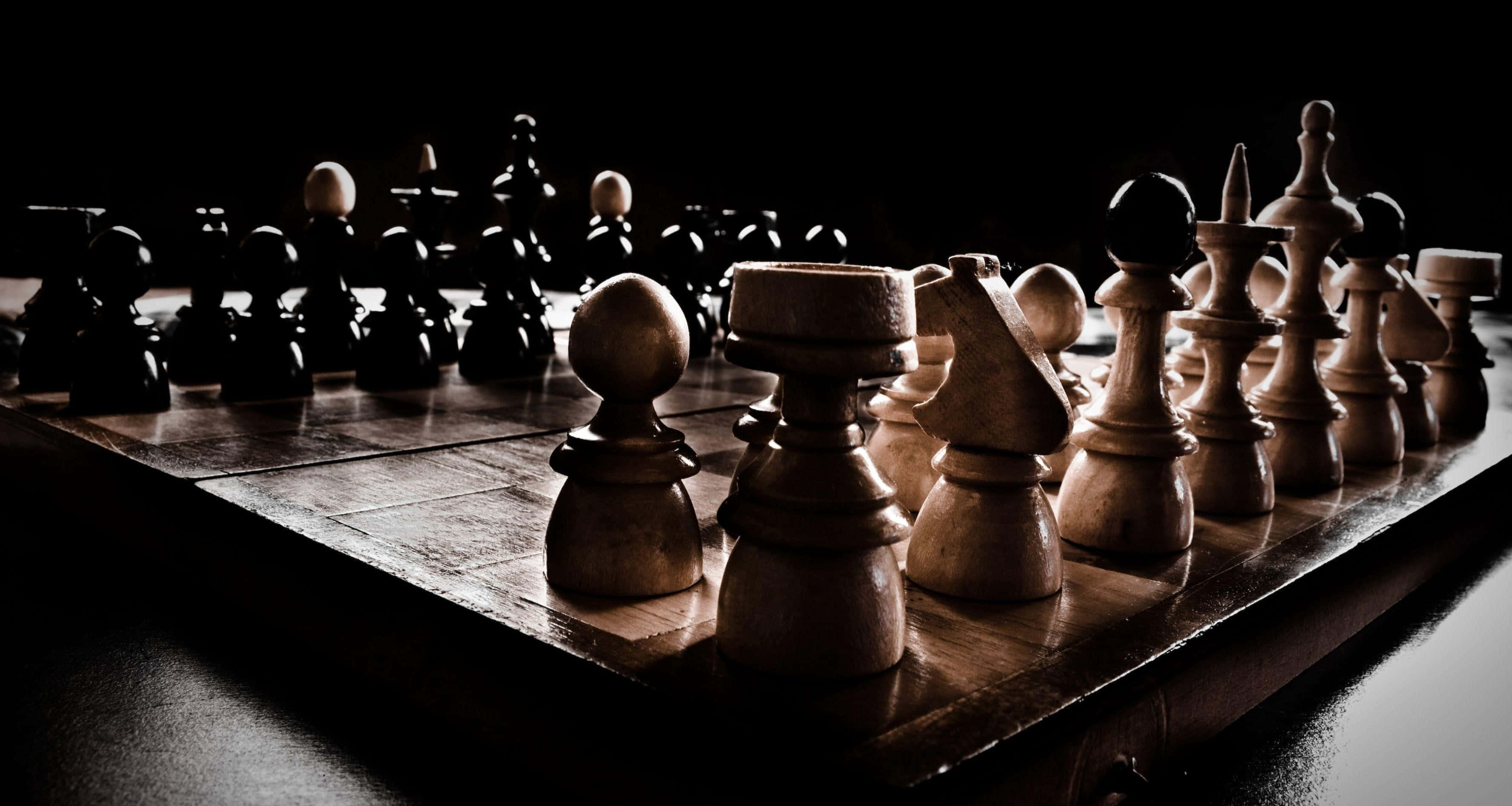 國際象棋 桌布 壁紙 — 一個戲劇性的低角度拍攝，木製國際象棋棋子放在棋盤上，在強烈的聚光燈下，背景為黑色。
