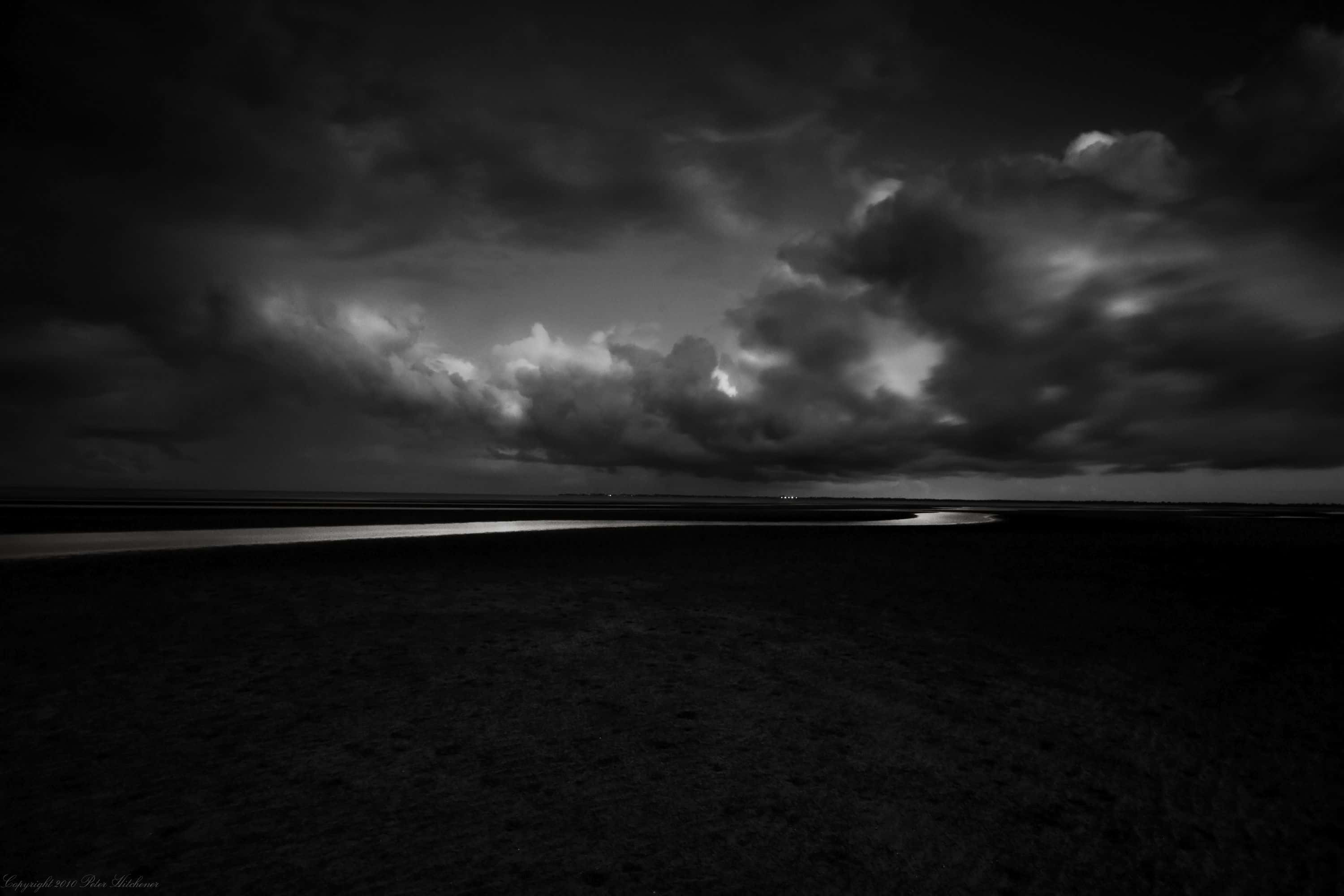 Dark Landscape 桌布 壁紙 — 一個戲劇性的單色景觀，暴風雨的天空籠罩著黑暗的濕地，有一條蜿蜒的水道。