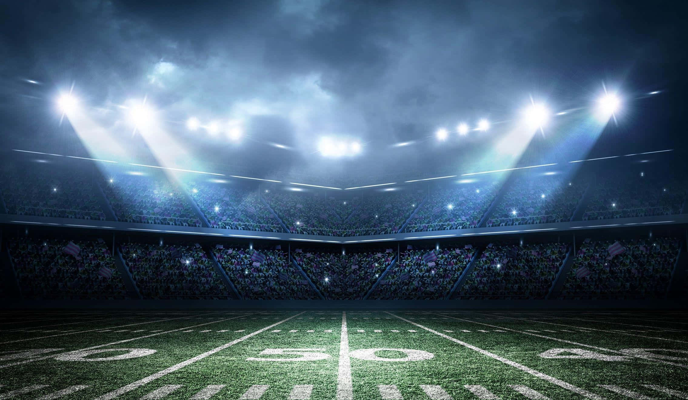 Football Stadium 桌布 壁紙 — 一個戲劇性的夜間足球場，被明亮的聚光燈照亮，穿過風暴雲層，照耀著擠滿的人群。
