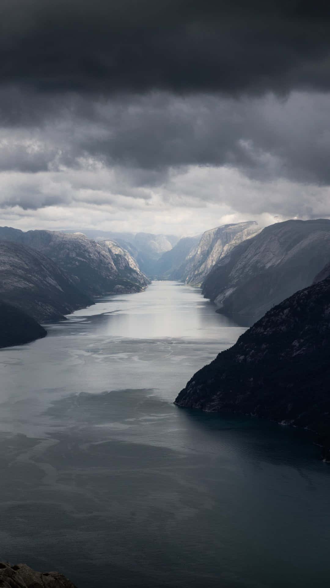 Norway 桌布 壁紙 — 一個戲劇性的峽灣在陰沉天空下蜿蜒於高聳陰暗的山脈之間。