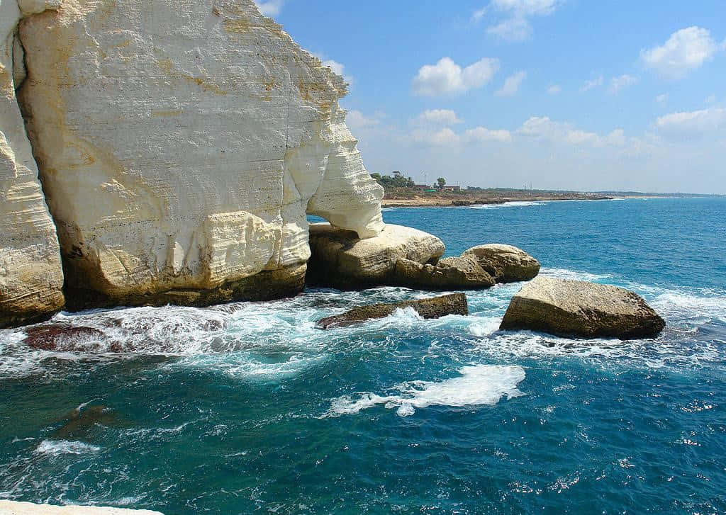 Israel 桌布 壁紙 — 一個戲劇性的海岸場景，高聳的白色懸崖與碧綠的海水相遇，天空湛藍，白雲點綴。