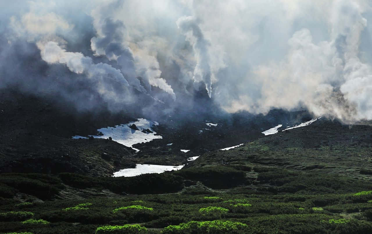 Breathtaking 桌布 壁紙 — 一個戲劇性的火山景觀，煙霧從多山的地形中升起，地形上點綴著斑塊的雪和充滿活力的綠色植被。