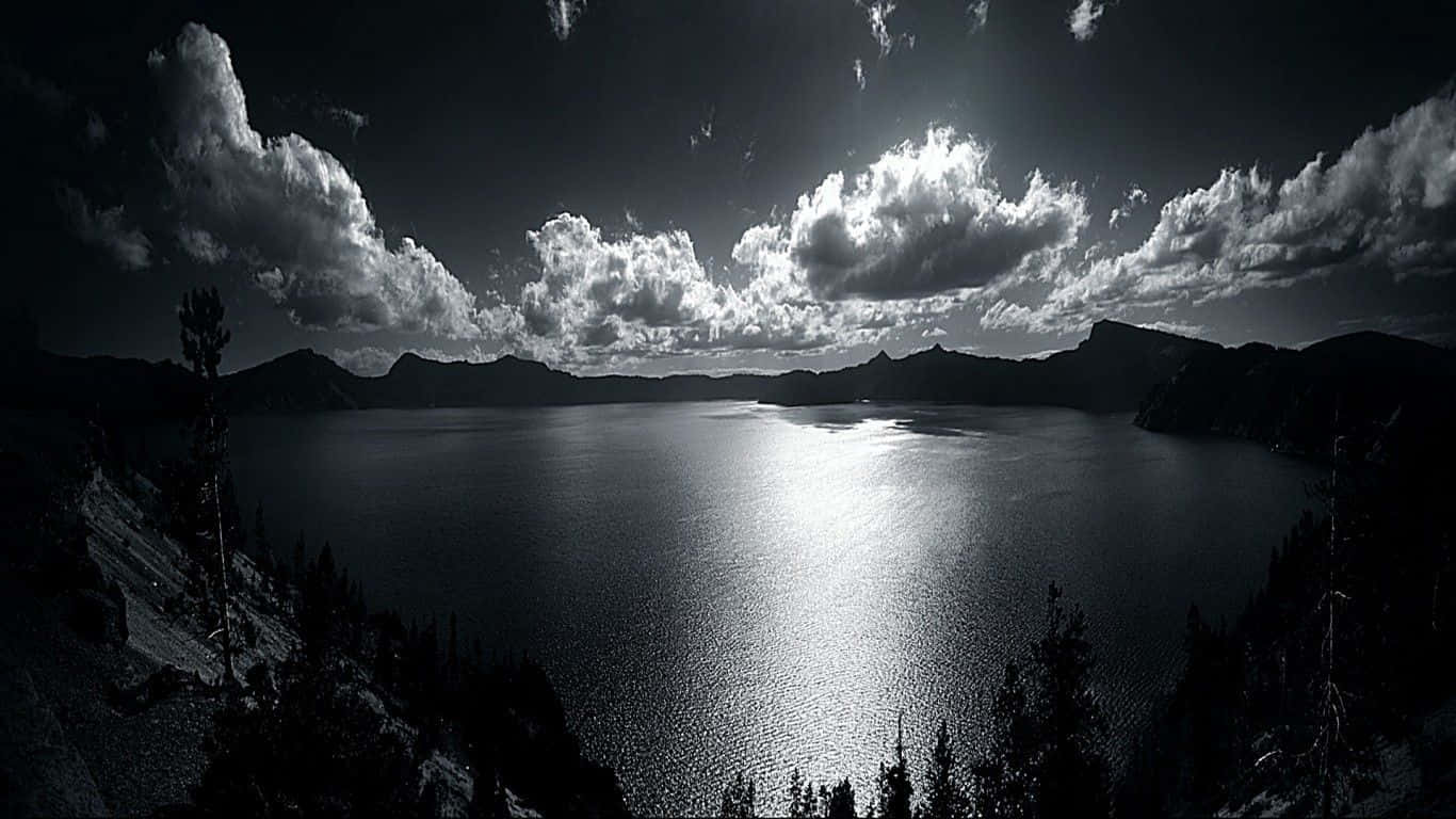 Dark Sky 桌布 壁紙 — 一個戲劇性的黑白景色，廣闊的火山口湖映照著陽光照射的雲朵，襯托著黑暗的山脈輪廓。