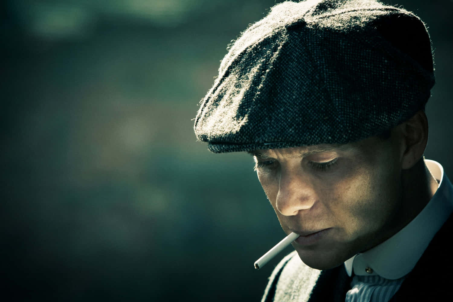 Peaky Blinders 桌布 壁紙 — 一個戴平頂帽的男人在模糊的綠色背景下抽煙，表情陰沉。