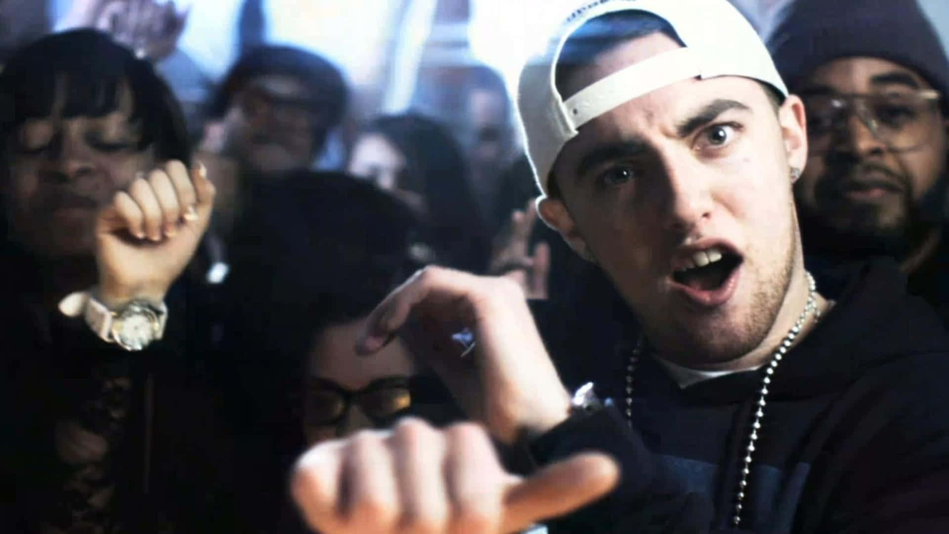 Mac Miller 桌布 壁紙 — 一個戴白色帽嘅年輕男子喺昏暗場地入面被人群包圍，表情強烈咁指向前面。