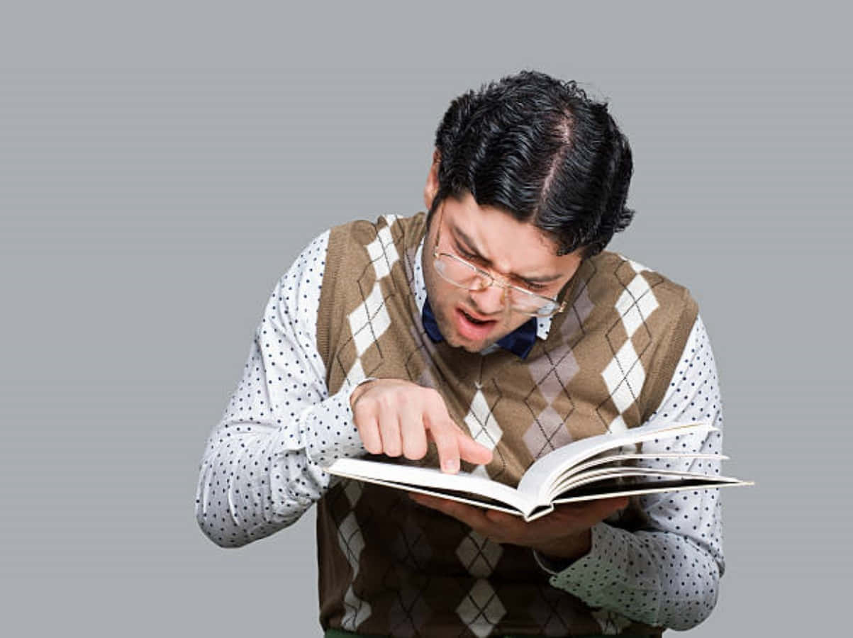 書呆子 桌布 壁紙 — 一個戴眼鏡、身穿棕色菱形花紋背心的男人，指著一本書，表情震驚。