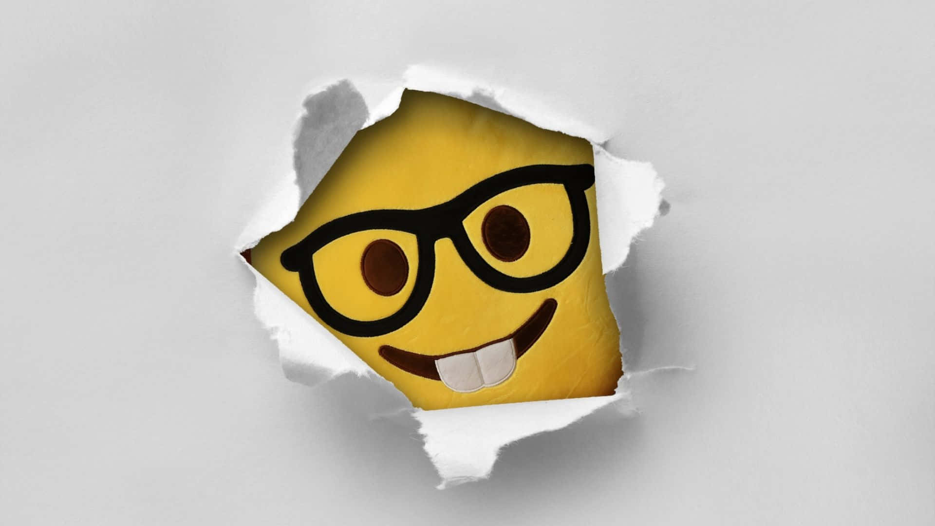 Smiley 桌布 壁紙 — 一個戴眼鏡嘅開心黃色表情符號，從撕爛嘅白色紙窿度偷望出嚟。