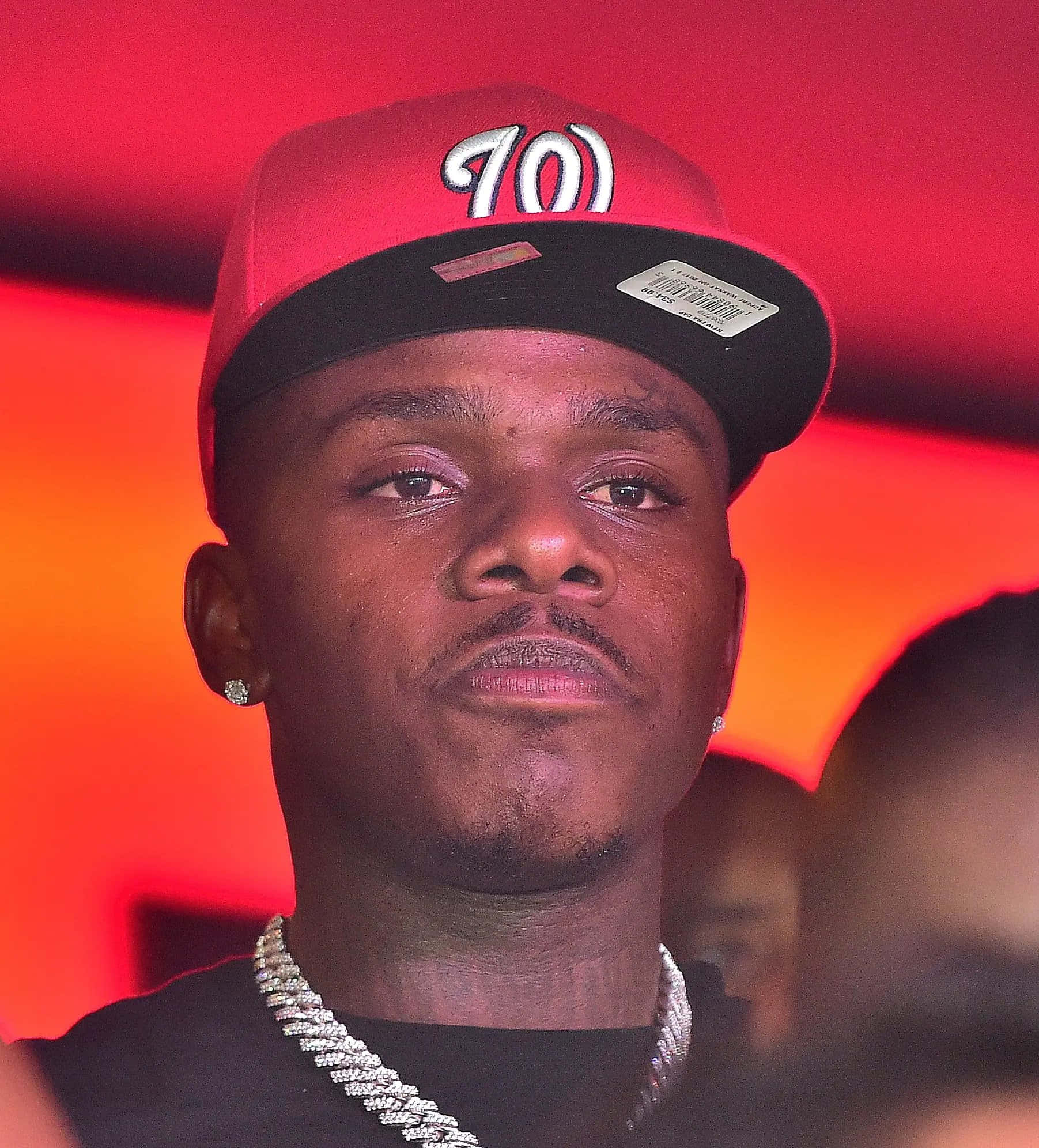 Dababy 桌布 壁紙 — 一個戴着印有「701」的紅黑色帽子和粗鏈條的男人，在發光的紅橙色背景下凝視着。