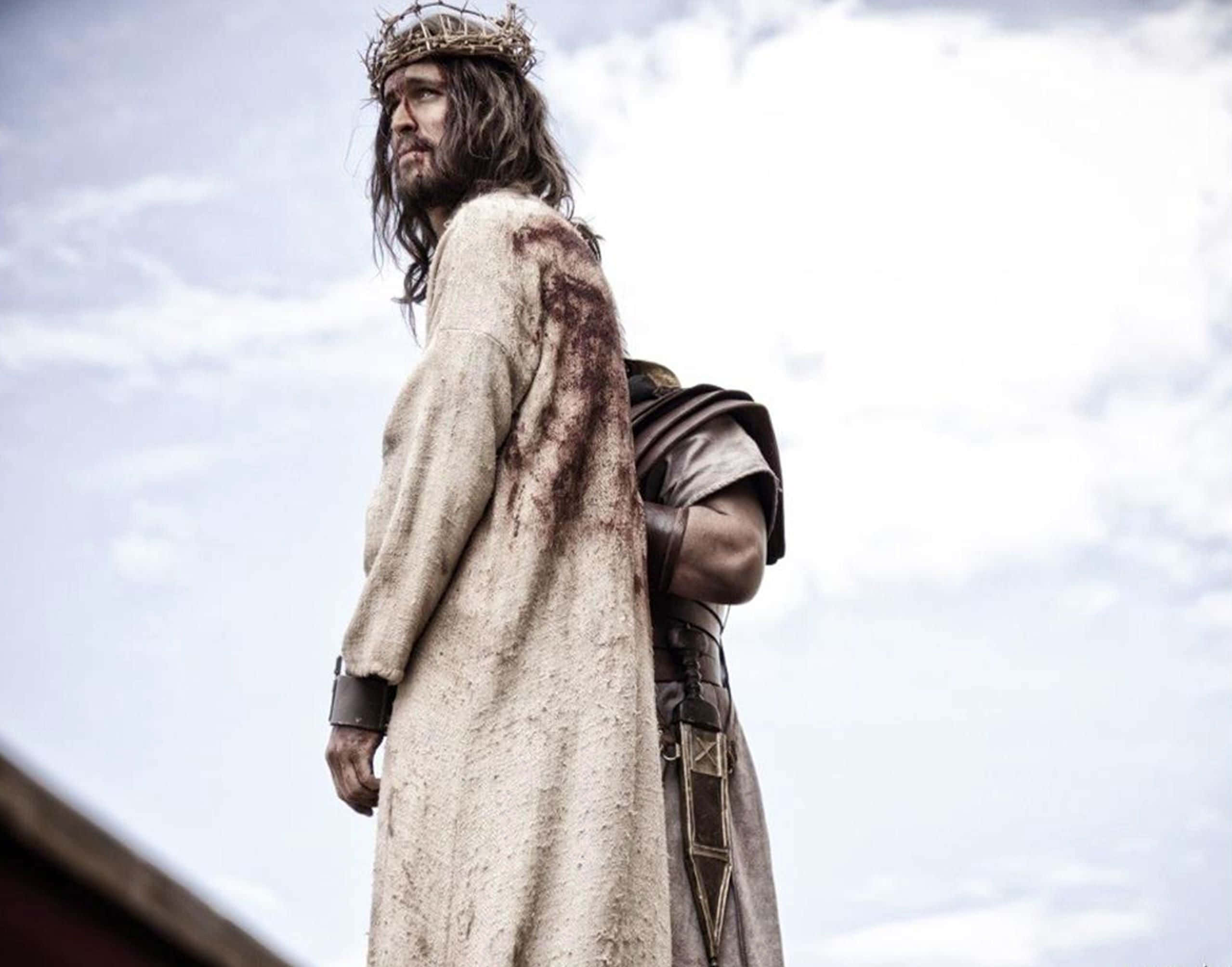 Son Of God 桌布 壁紙 — 一個戴着荊棘冠冕、身穿血跡斑斑長袍的男子，在陰雲密佈的天空下莊嚴地站立。