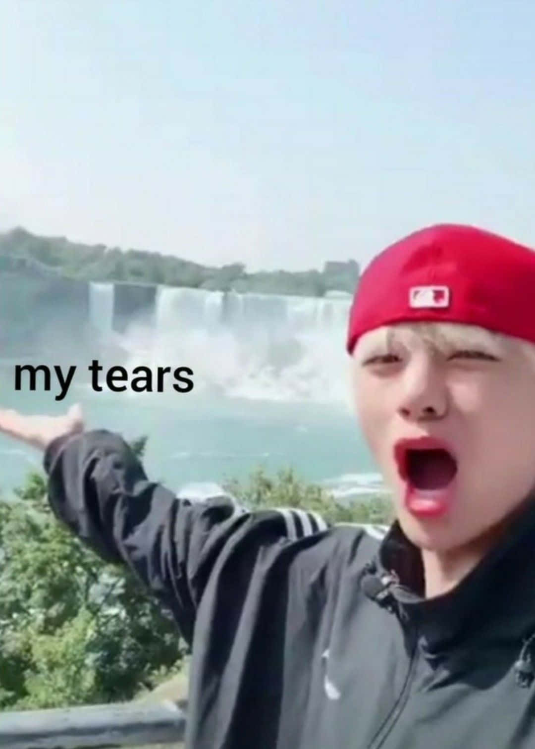 Bts Meme 桌布 壁紙 — 一個戴紅帽嘅人企喺一個巨大瀑布前面，雙臂張開，嘴巴張開，充滿敬畏。