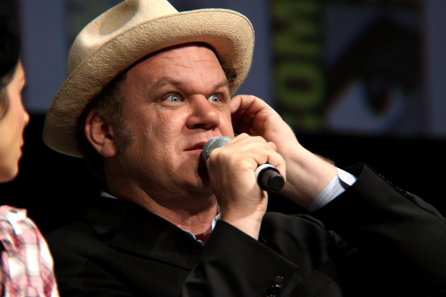 John C. Reilly 桌布 壁紙 — 一個戴草帽嘅男人喺小組討論期間，瞪大眼、表情驚訝噉揸住支咪。