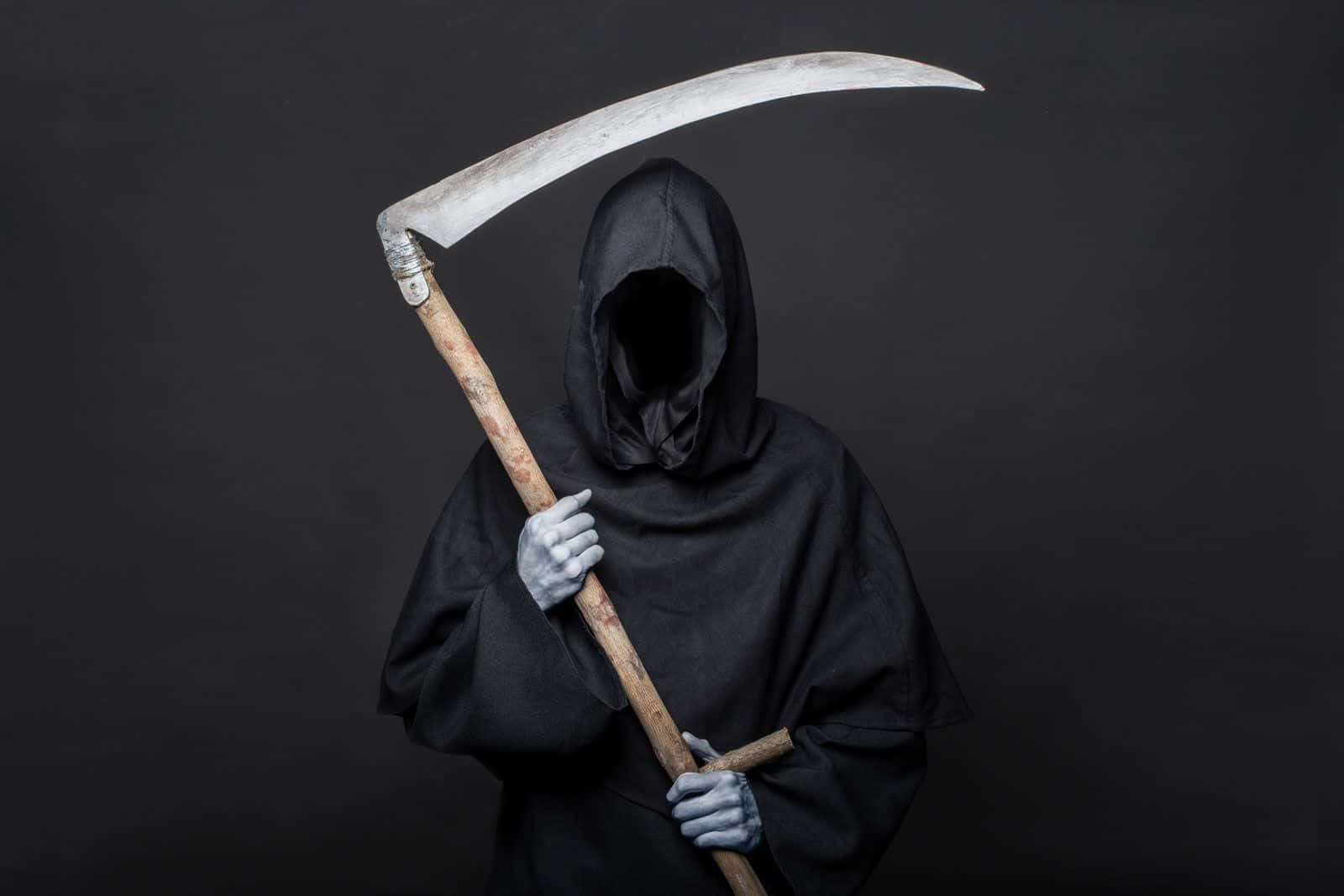 死神 桌布 壁紙 — 一個戴著兜帽、雙手蒼白的死神，在深灰色背景上握著一把生鏽的鐮刀。