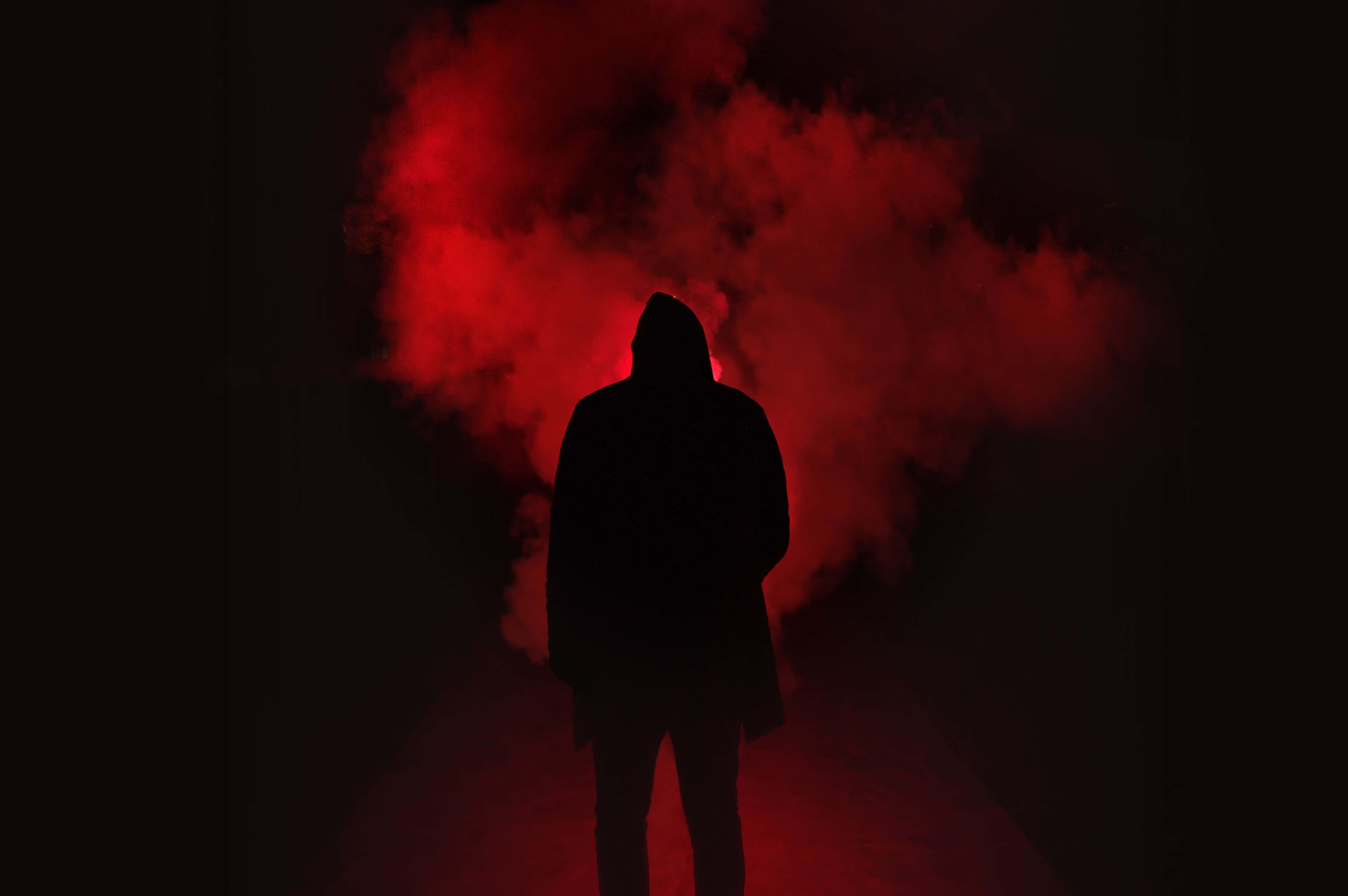 Silhouette 桌布 壁紙 — 一個戴著兜帽的身影在黑暗虛空中以旋轉的紅色煙霧背景呈現剪影。