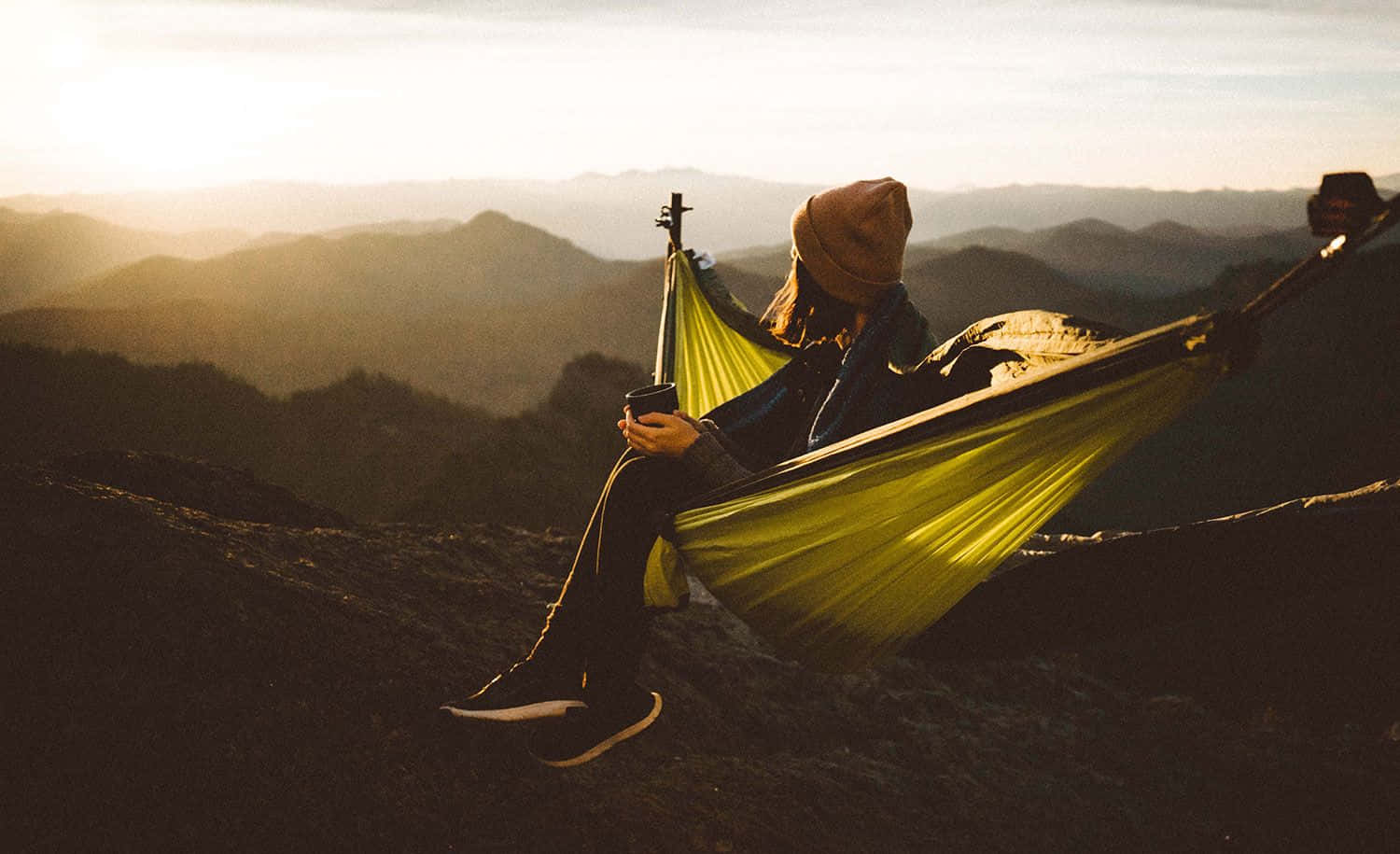 Minimalist Camping 桌布 壁紙 — 一個戴著冷帽嘅人喺金色時刻，喺懸掛喺山脊上嘅亮黃色吊床上放鬆。