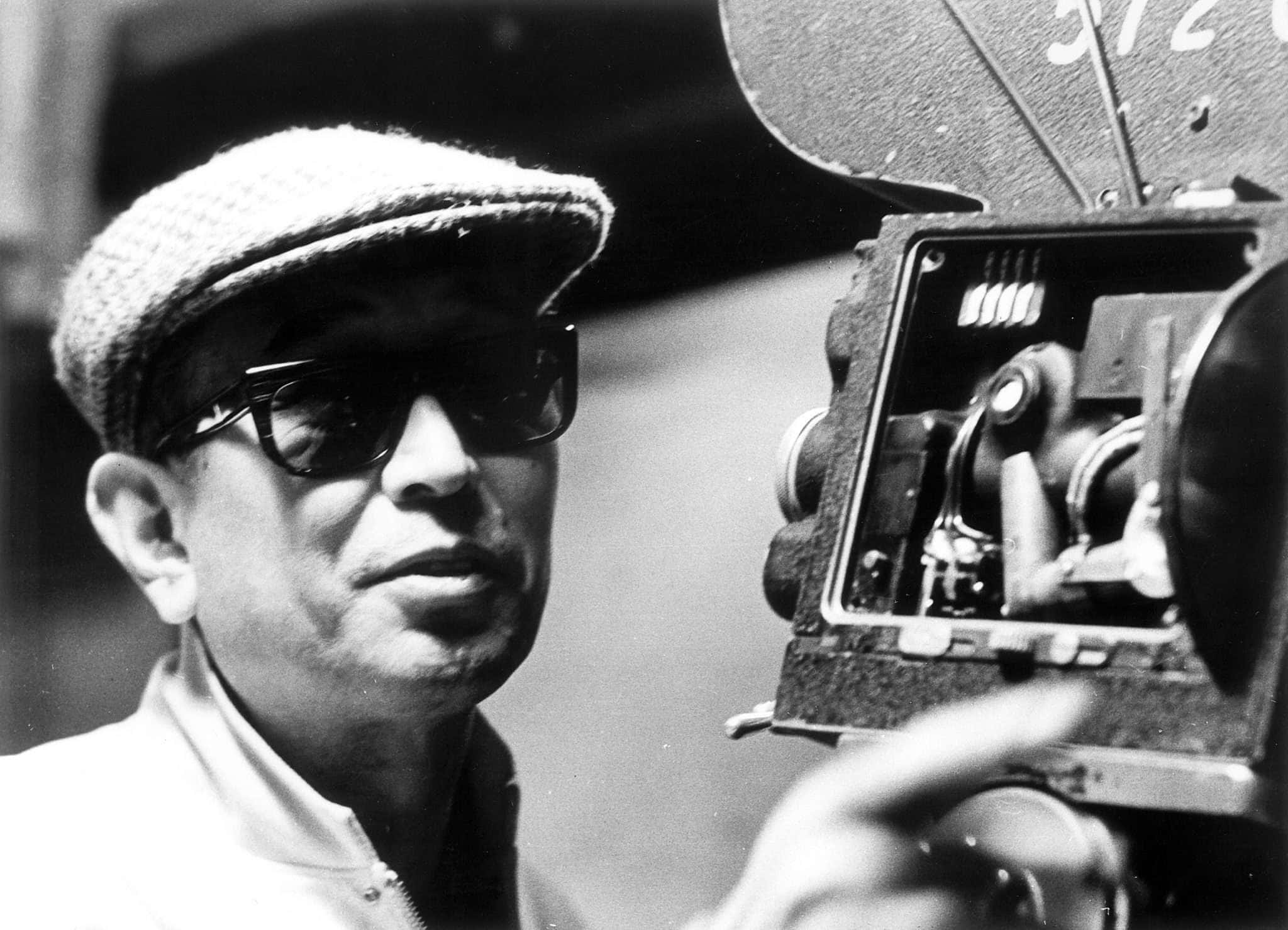 Akira Kurosawa 桌布 壁紙 — 一個戴著帽子和太陽眼鏡的男人操作復古菲林相機的黑白肖像。
