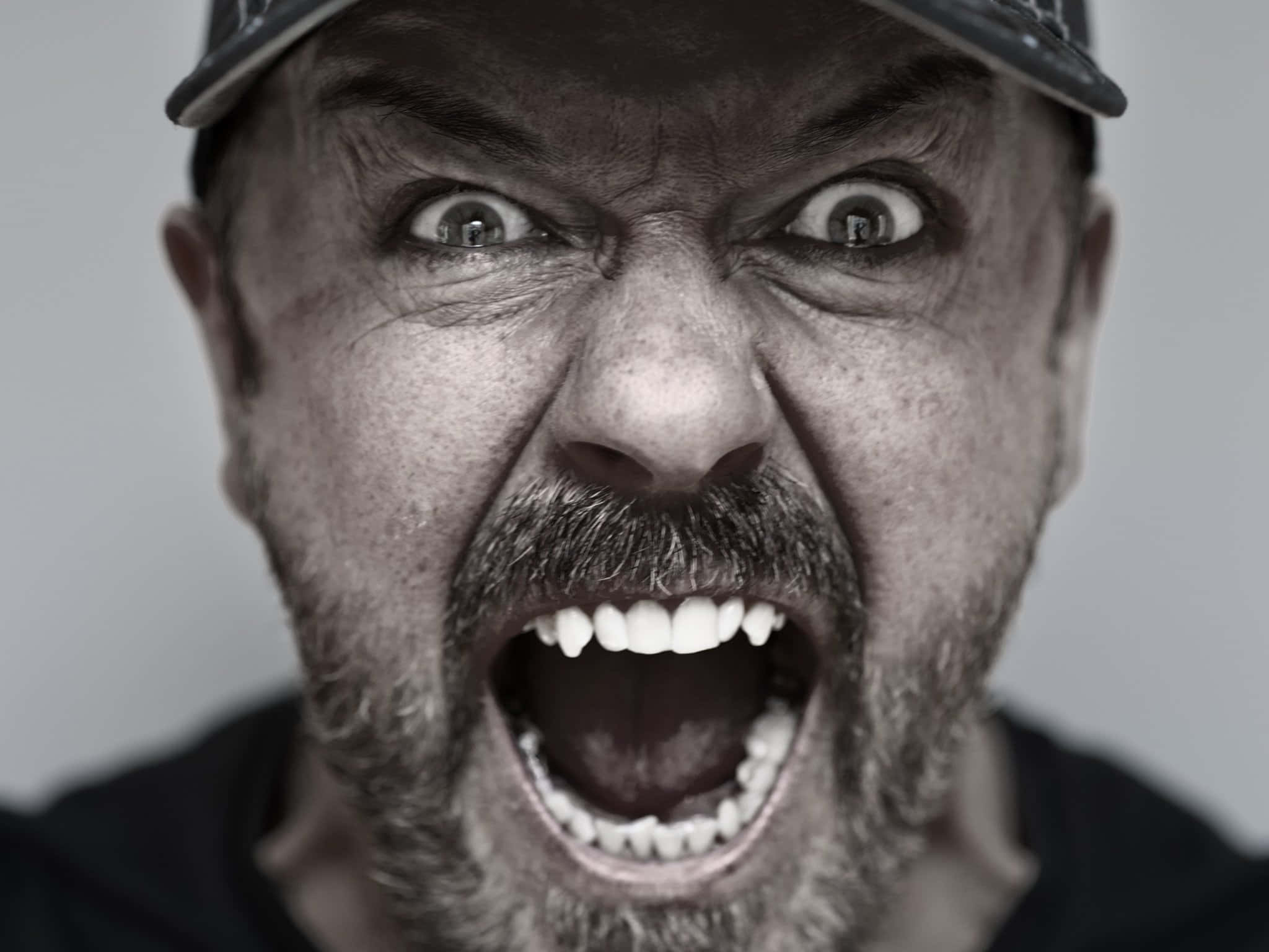 ricky gervais 桌布 壁紙 — 一個戴著帽子的男人，睜大眼睛、露出牙齒尖叫，以鮮明的黑白特寫呈現。