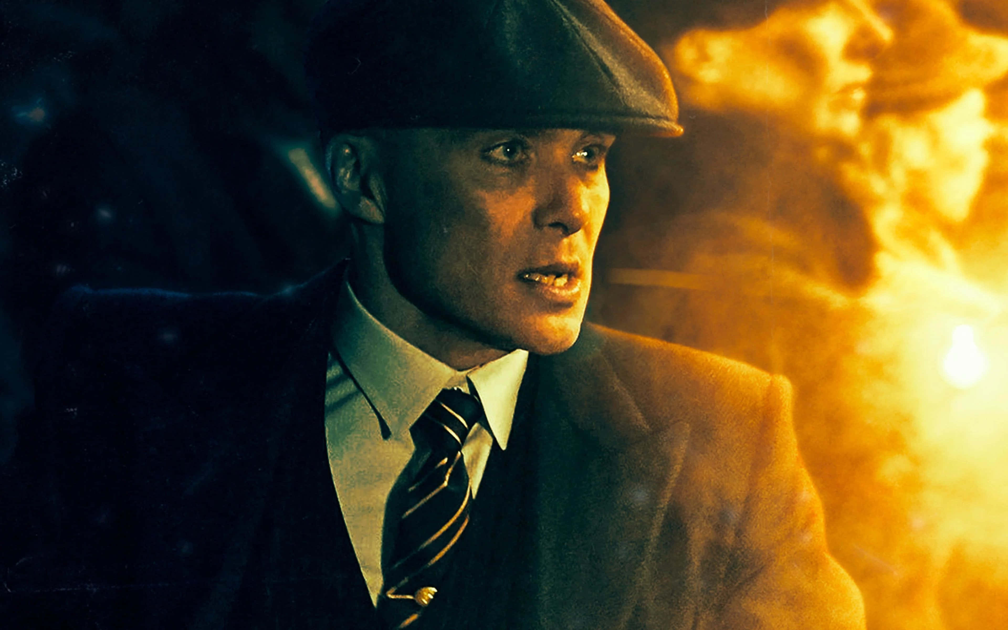 Peaky Blinders 桌布 壁紙 — 一個戴著平頂帽和西裝的男人，在熾熱的橙色爆炸背景下凝視著。