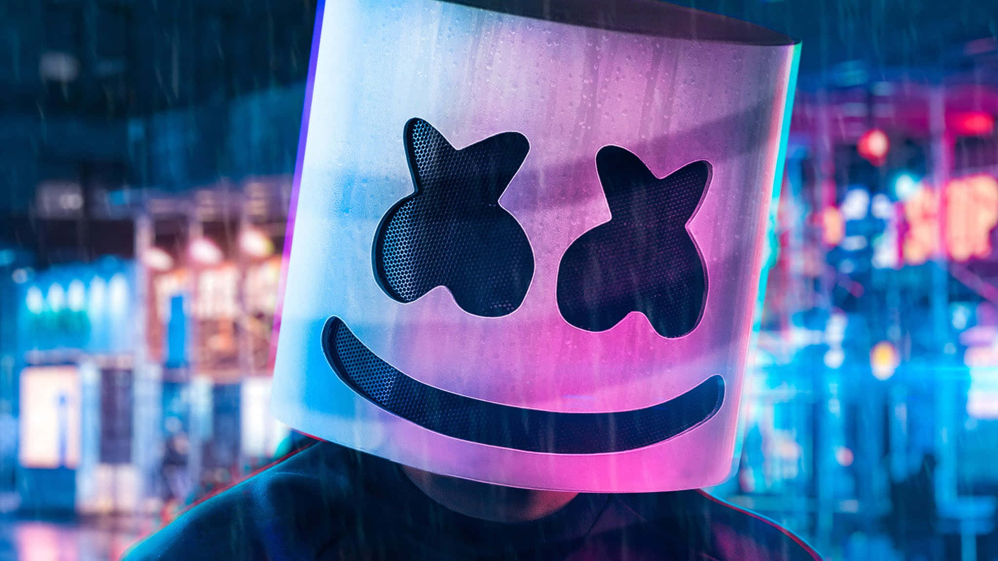 Marshmello 桌布 壁紙 — 一個戴著發光Marshmello面具的人，夜晚站在被雨水浸透、霓虹燈閃爍的城市街道上。