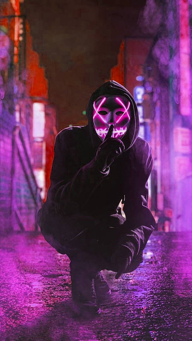 戴著發光面具的人夜晚蹲在霓虹燈照亮、下雨的小巷中。 — 螢光紫 壁紙