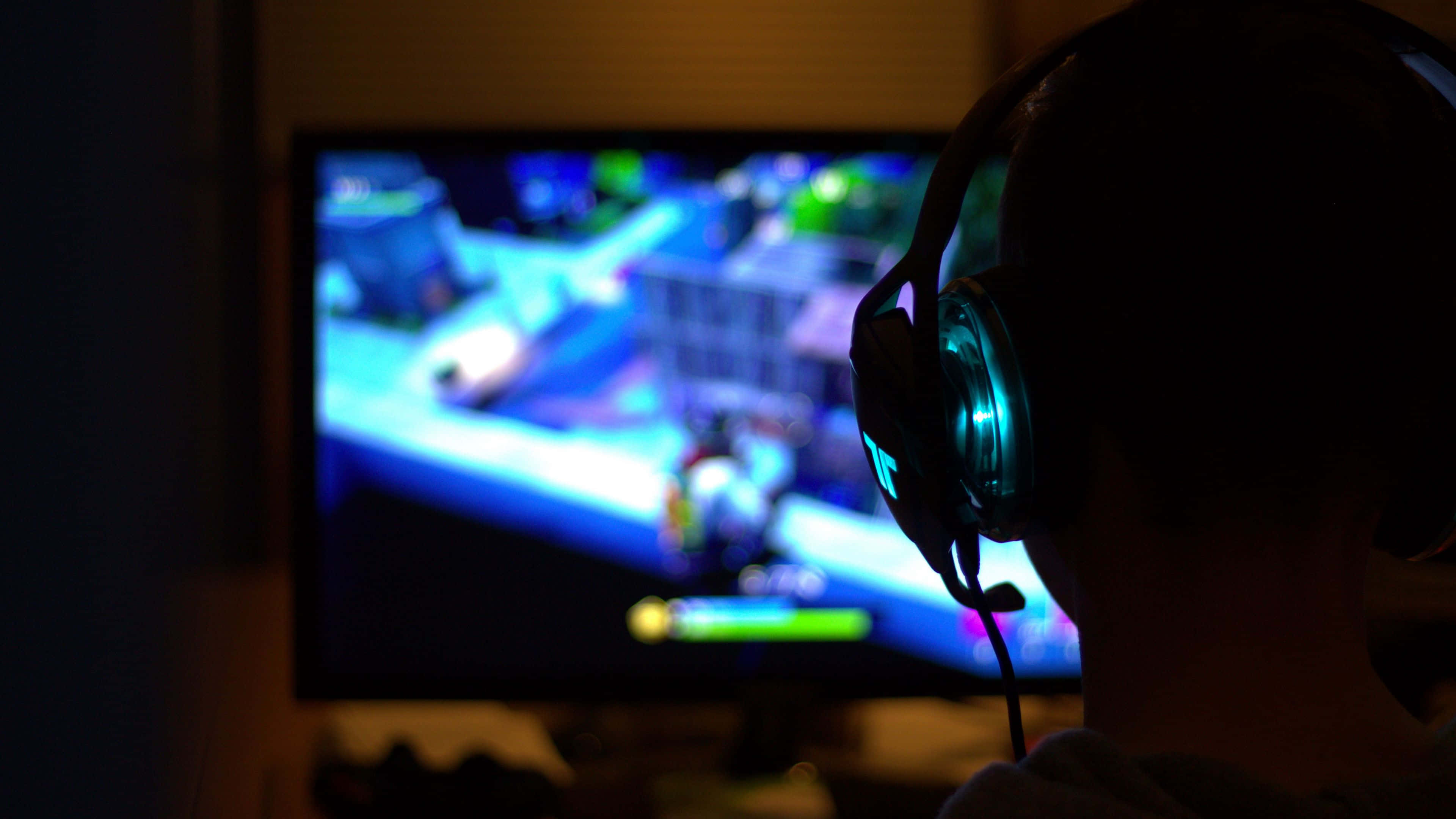 Dark Gaming 桌布 壁紙 — 一個戴著發光耳機的遊戲玩家剪影，在昏暗的房間中專注於充滿活力的藍色和綠色視頻遊戲屏幕。
