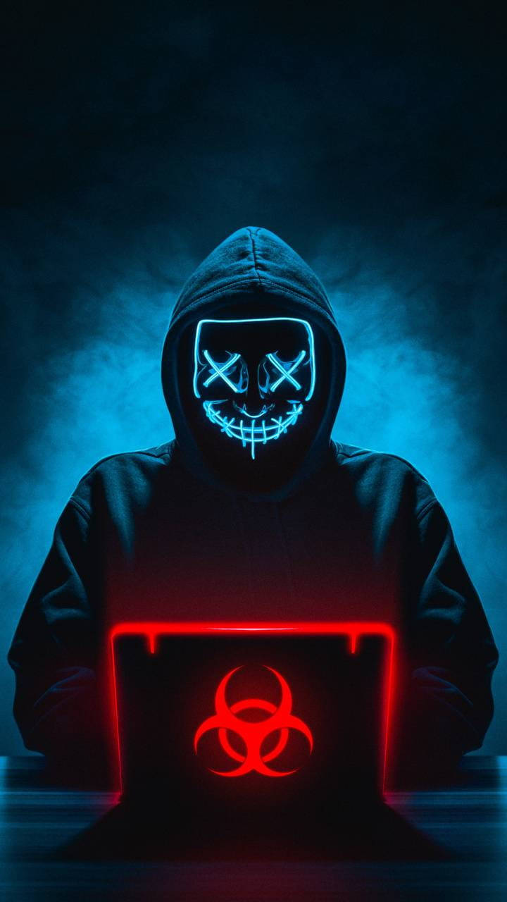 Hacking 桌布 壁紙 — 一個戴著發光藍色面具的兜帽人物坐在陰暗的藍色煙霧中，使用一台顯示紅色生物危害符號的筆記型電腦。