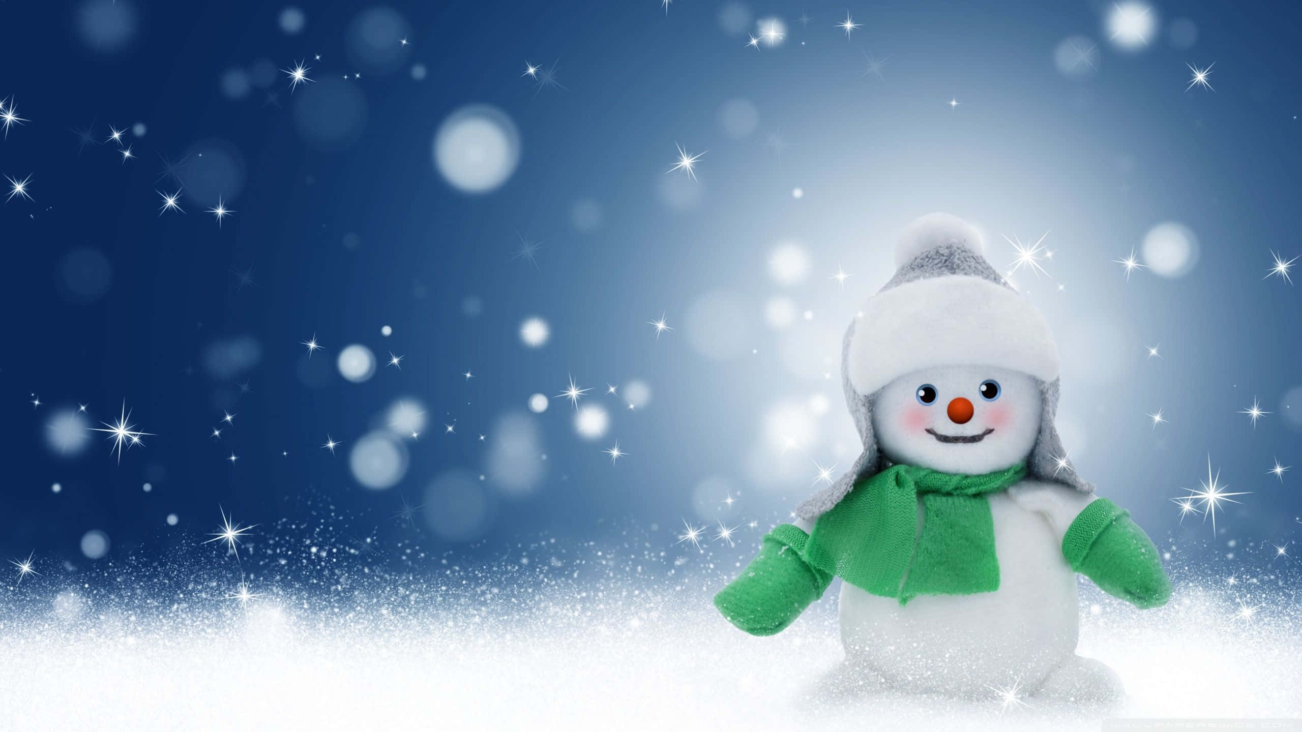 雪人 桌布 壁紙 — 一個戴著白色帽子和綠色圍巾的快樂雪人，站在飄落的雪花中，背景是閃爍的藍色冬夜天空。