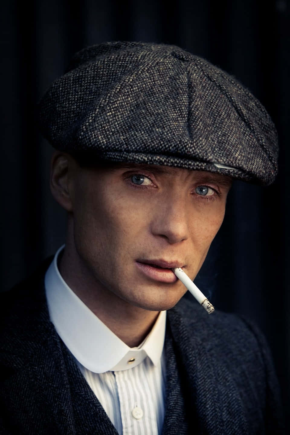 Peaky Blinders 桌布 壁紙 — 一個戴著粗花呢平頂帽、身穿西裝的男人，在黑暗背景下神情嚴肅地拿著一支香煙。