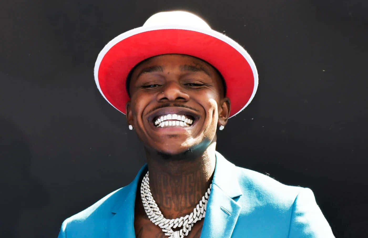Dababy 桌布 壁紙 — 一個戴著紅白帽子和藍色西裝的男人在深色背景下大笑。
