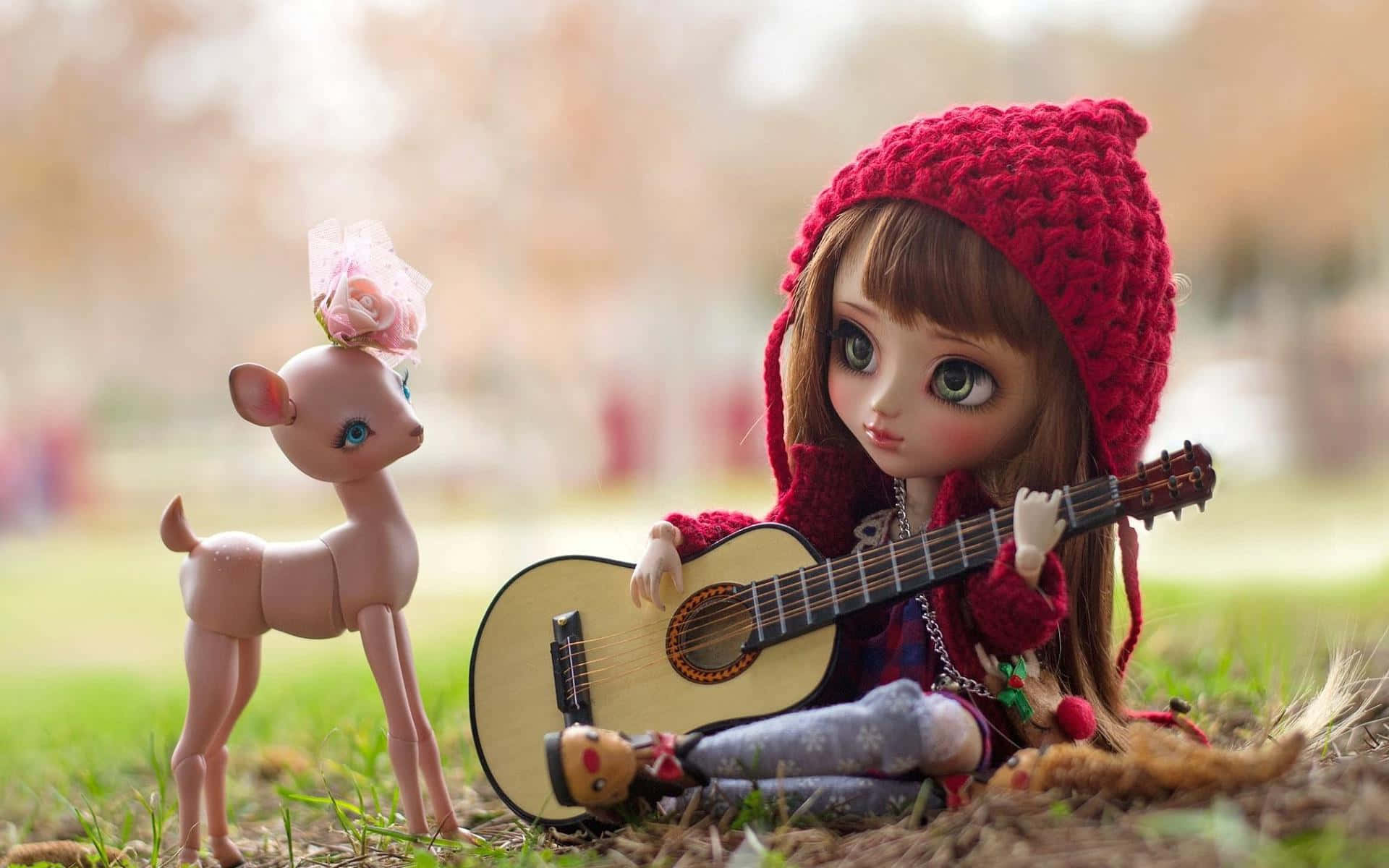 toys 桌布 壁紙 — 一個戴著紅色針織帽子的公仔坐在草地上彈結他，旁邊有一個頭上有粉紅色玫瑰的小鹿公仔。