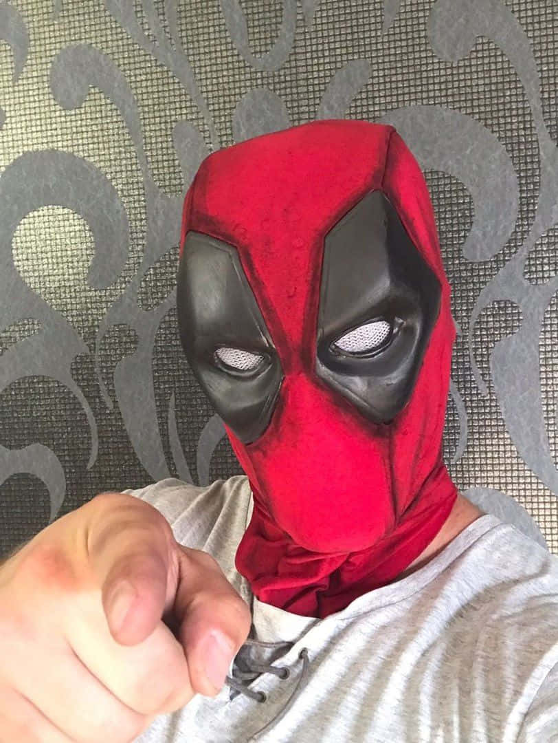 Deadpool Mask 桌布 壁紙 — 一個戴著紅黑色死侍面具的人直接指向鏡頭，背景是灰色圖案牆紙。
