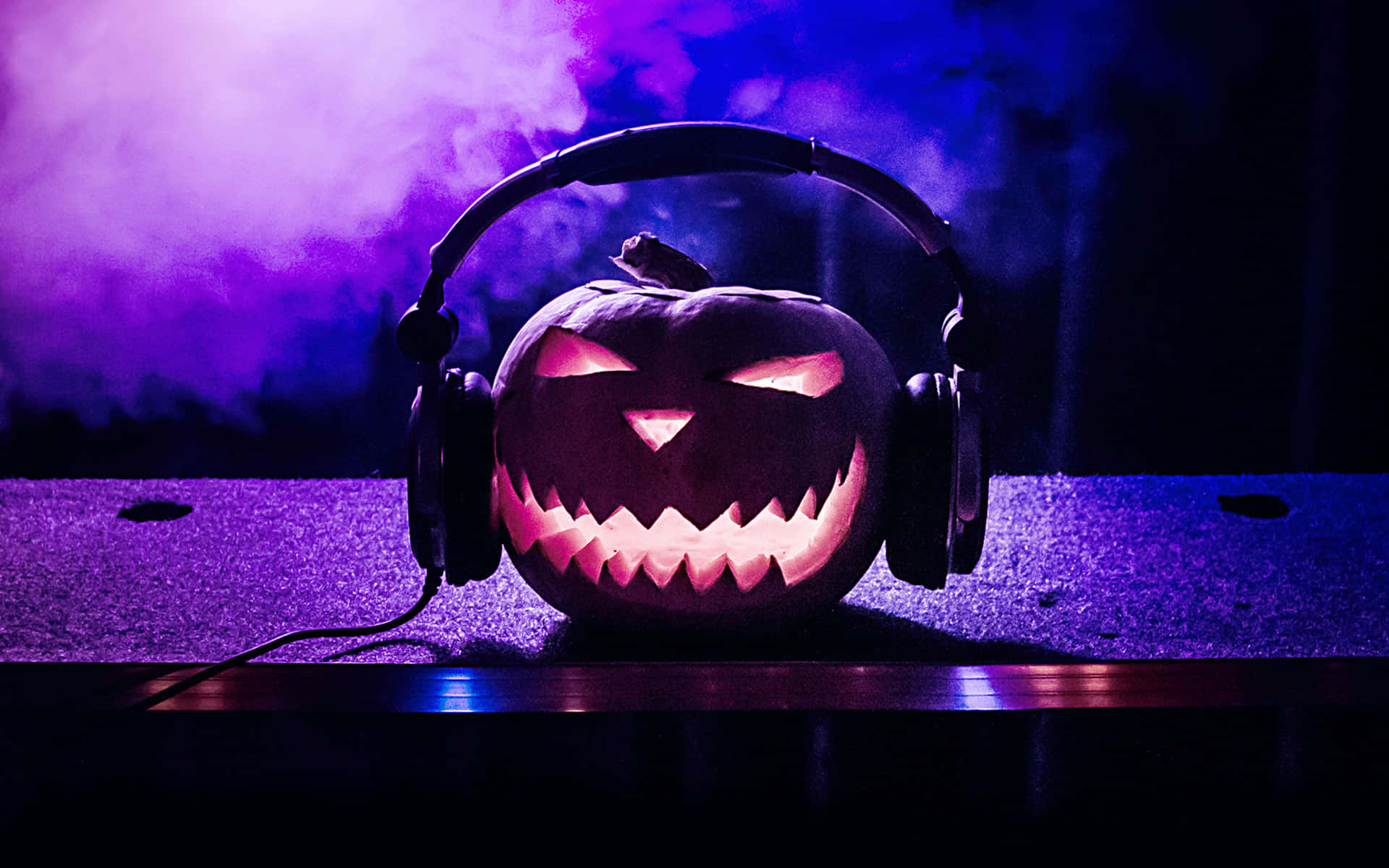 Halloween Music 桌布 壁紙 — 一個戴著耳機的發光南瓜燈坐在舞台上，周圍是紫色煙霧和燈光。
