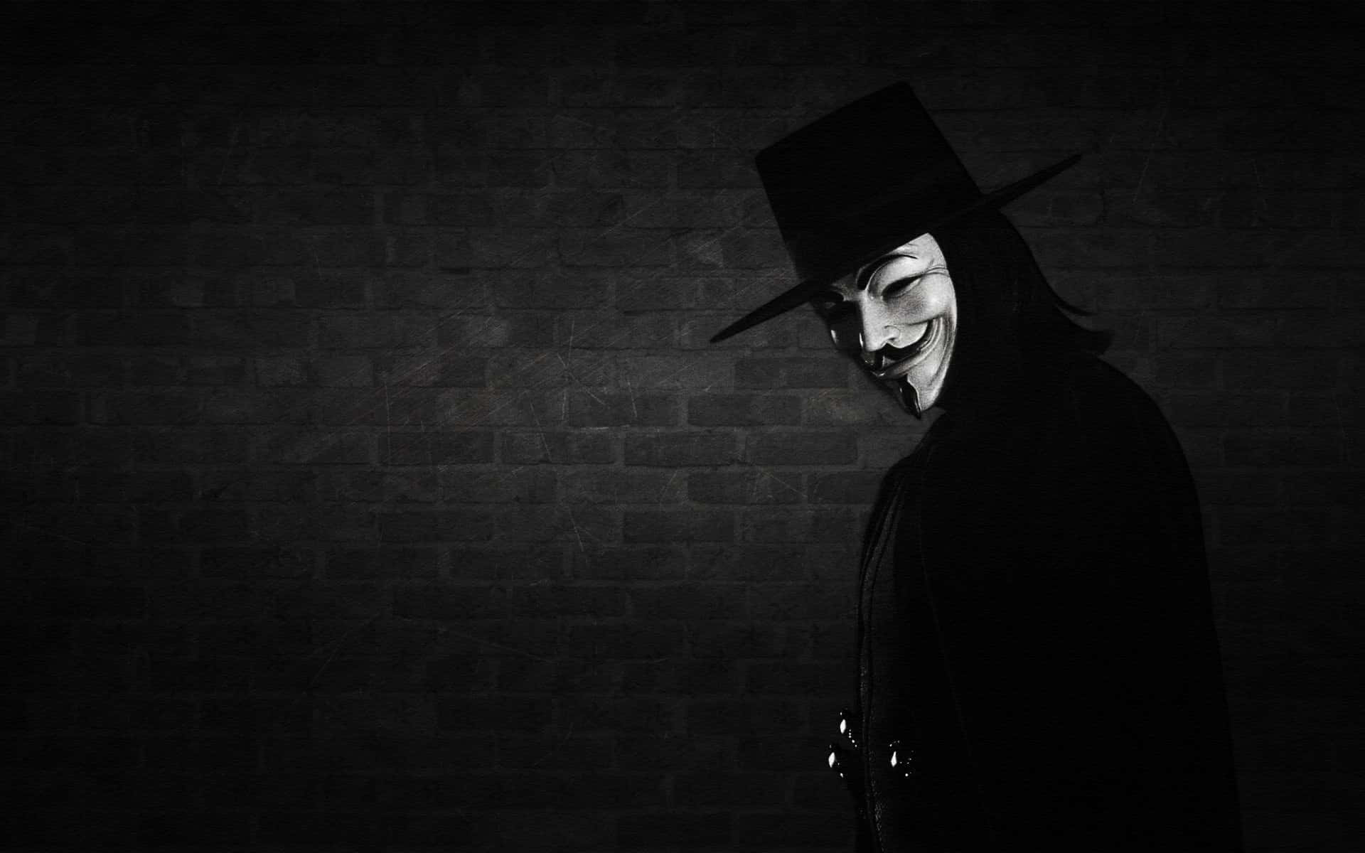 Anonymous 桌布 壁紙 — 一個戴著蓋伊·福克斯面具和寬邊帽的人物站在磚牆前的陰影中，被單一光源照亮。