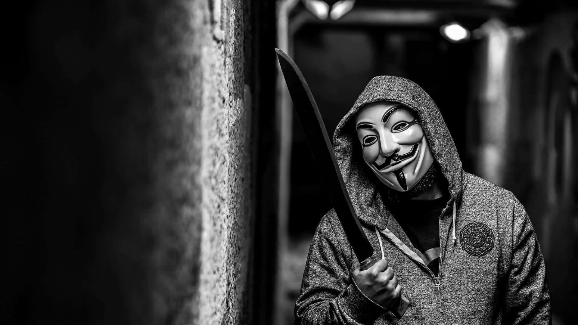 Anonymous 桌布 壁紙 — 一個戴著蓋伊·福克斯面具和連帽衫的人，在光線昏暗的城市小巷中拿著一把大刀。
