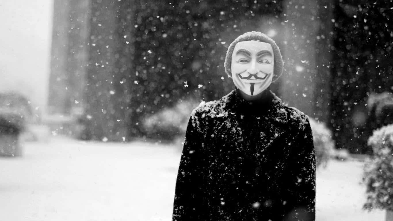 Anonymous 桌布 壁紙 — 一個戴著蓋伊·福克斯面具的人站在飄雪中，背景是模糊的樹木。
