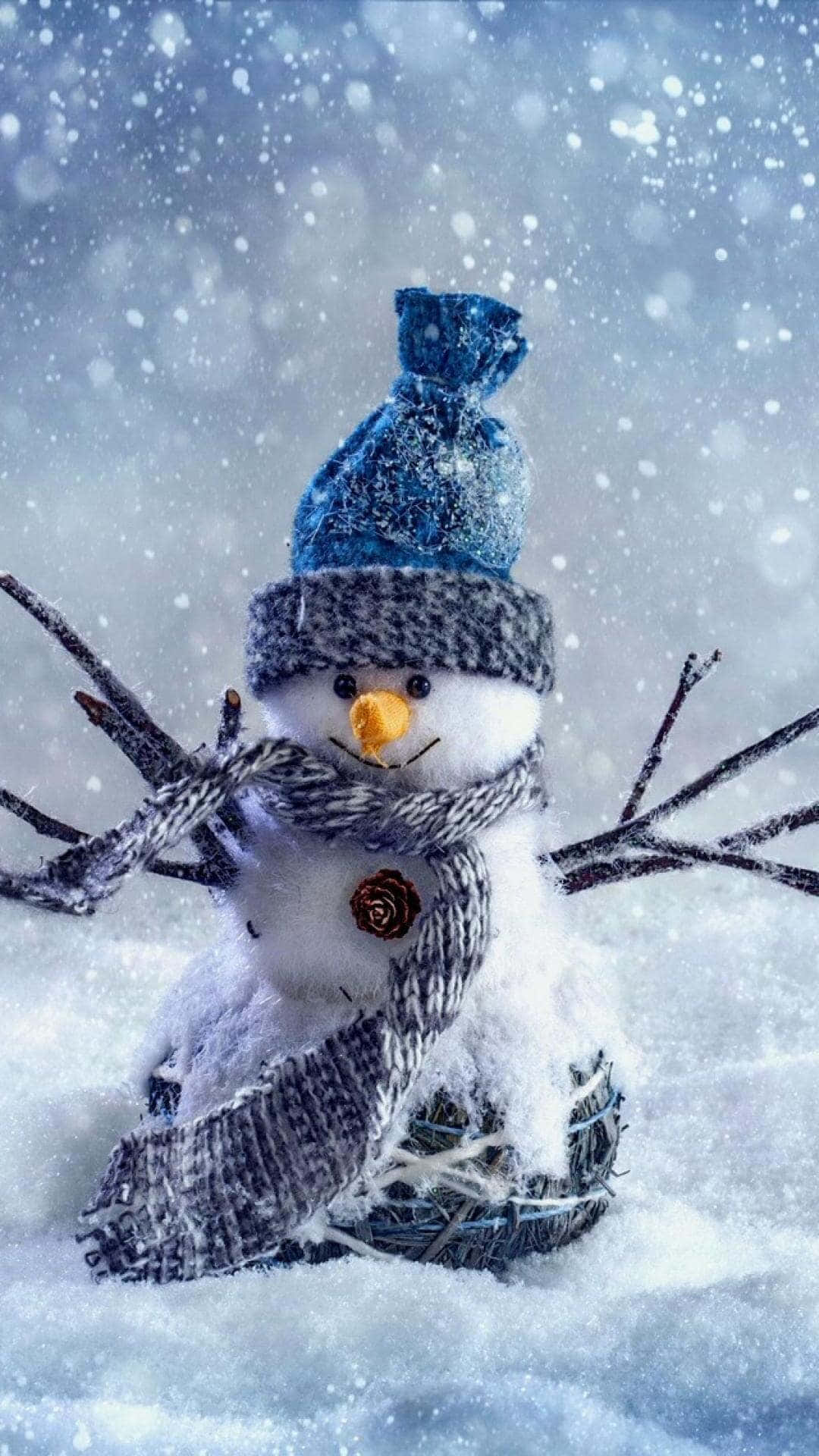 Cute Winter Aesthetic 桌布 壁紙 — 一個戴著藍色帽子和條紋圍巾的快樂雪人，用樹枝手臂坐在飄雪中。