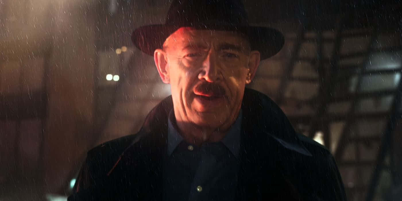 J Jonah Jameson 桌布 壁紙 — 一個戴著軟呢帽、穿著風衣的男人在溫暖的路燈下站在雨中，表情嚴肅。