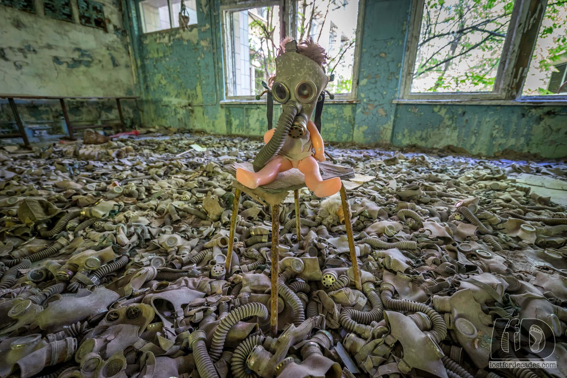 Chernobyl 桌布 壁紙 — 一個戴著防毒面具的洋娃娃坐在凳子上，周圍是成千上萬個被丟棄的防毒面具，房間的綠色牆壁正在腐朽。