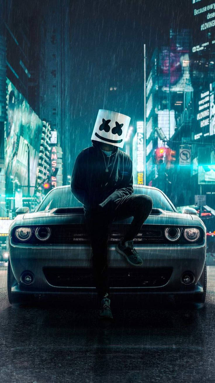 marshmello iPhone 桌布 壁紙 — 一個戴著面具的人物坐在一輛時尚肌肉車上，背景是雨夜霓虹閃爍的城市景觀。