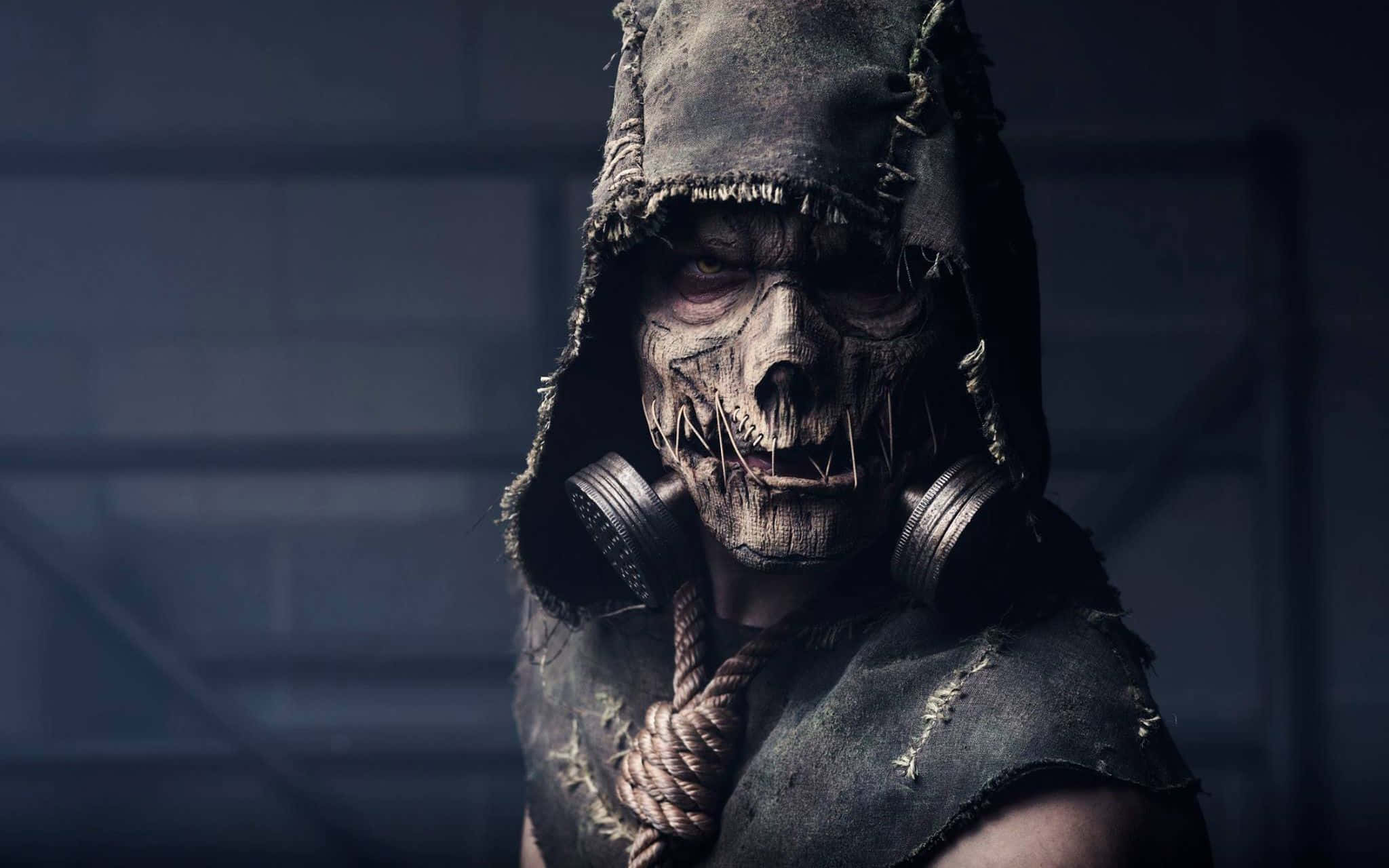 Horror Masks 桌布 壁紙 — 一個戴著頭骨面具和防毒面具的威脅性連帽人物，在昏暗的工業環境中凝視著。