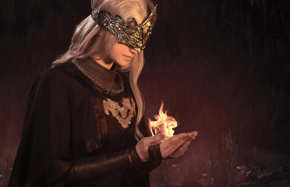 Fire Keeper 桌布 壁紙 — 一個戴面具、長銀色頭髮的人物，戴著手套的手上拿著一小團火焰，背景是黑暗的森林。