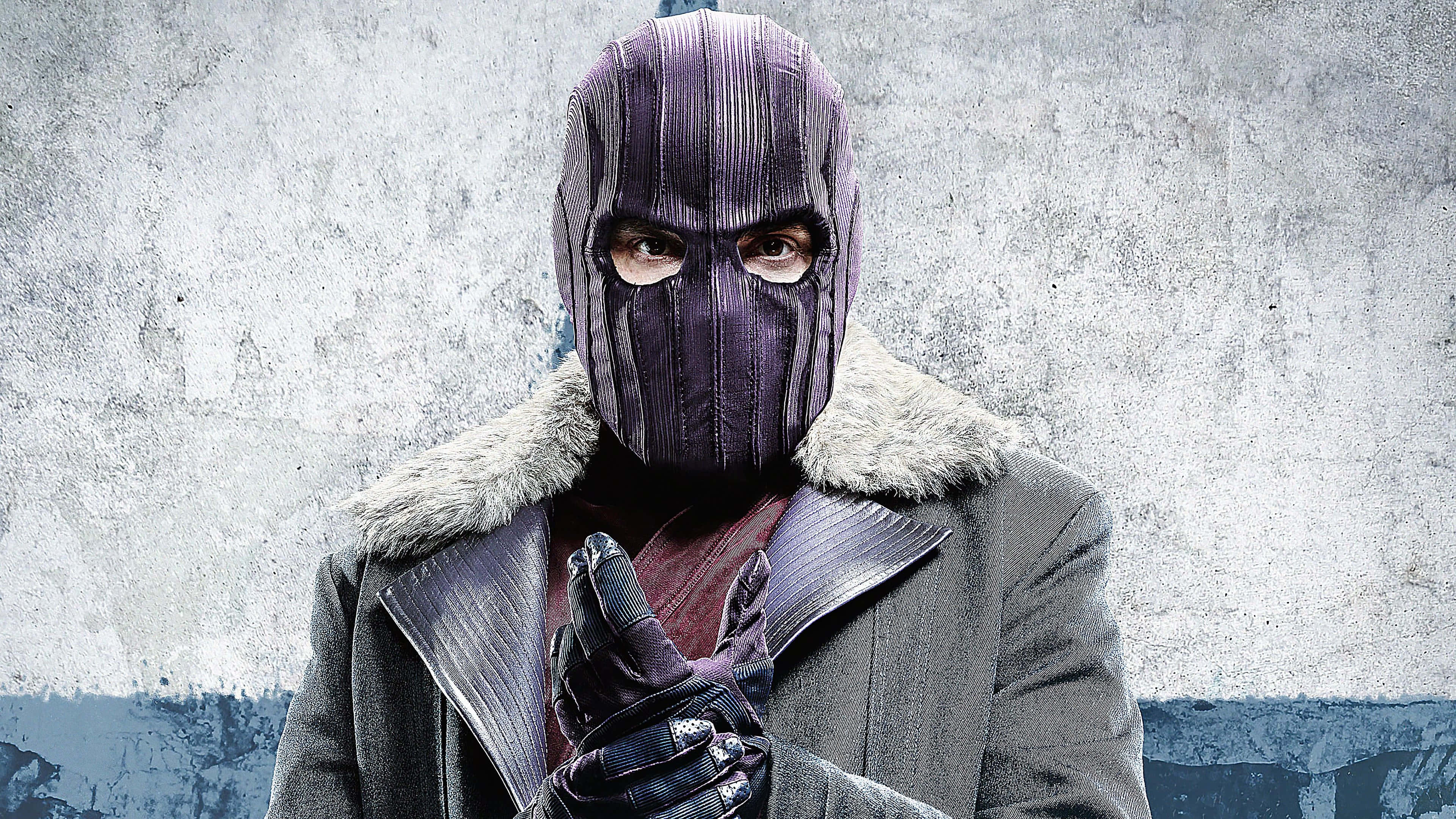 Baron Zemo 桌布 壁紙 — 一個戴面具的人物，身穿深色毛領大衣，靠著風化的混凝土牆站立，眼神銳利，雙手緊握。