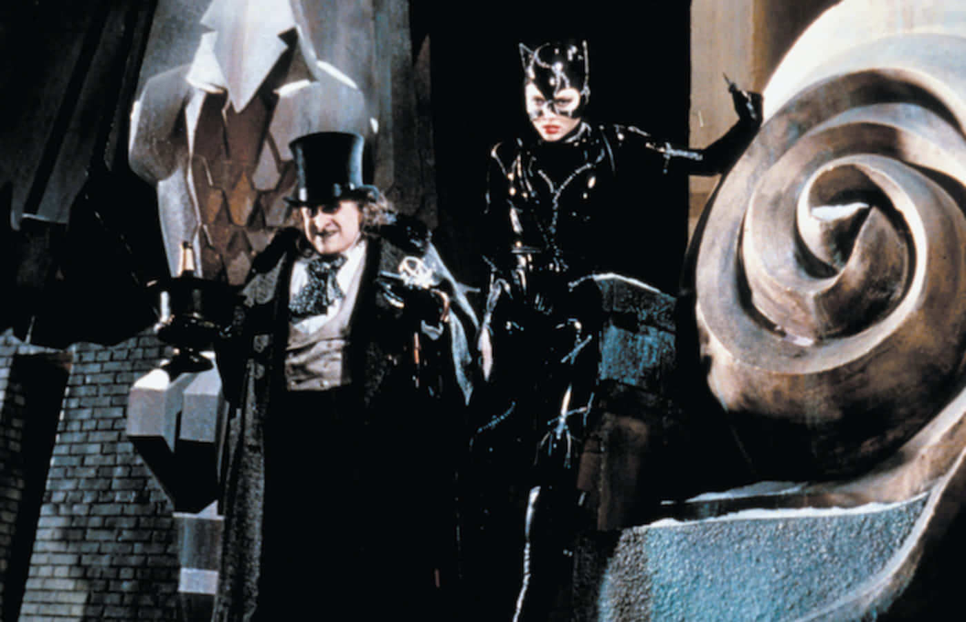 Batman Penguin 桌布 壁紙 — 一個戴高帽的威脅性反派站在一個戴面具的貓女旁邊，背景是黑暗哥德式風格，建築扭曲。