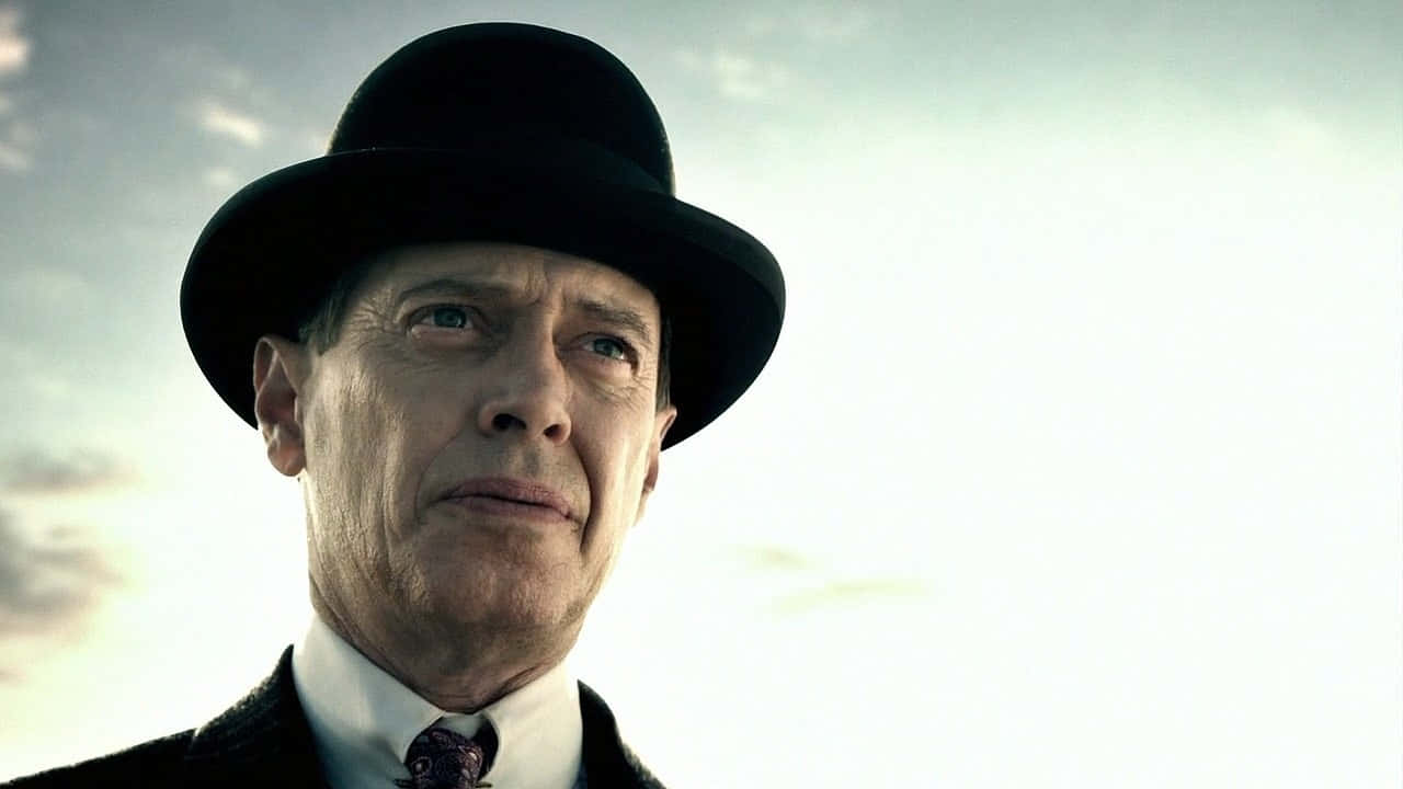 steve buscemi 桌布 壁紙 — 一個戴黑色圓頂禮帽、穿西裝的男人，在戲劇性光線下仰望多雲的天空。