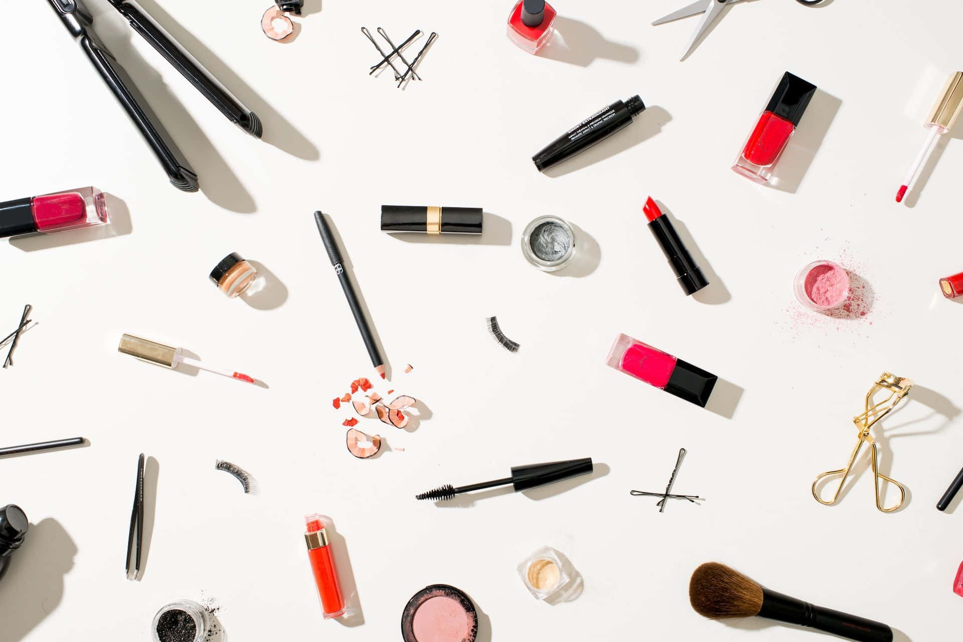 Cute Makeup 桌布 壁紙 — 一個扁平擺設，包含色彩鮮豔的化妝品和美容工具，散落在明亮的白色表面上，帶有強烈的陰影。